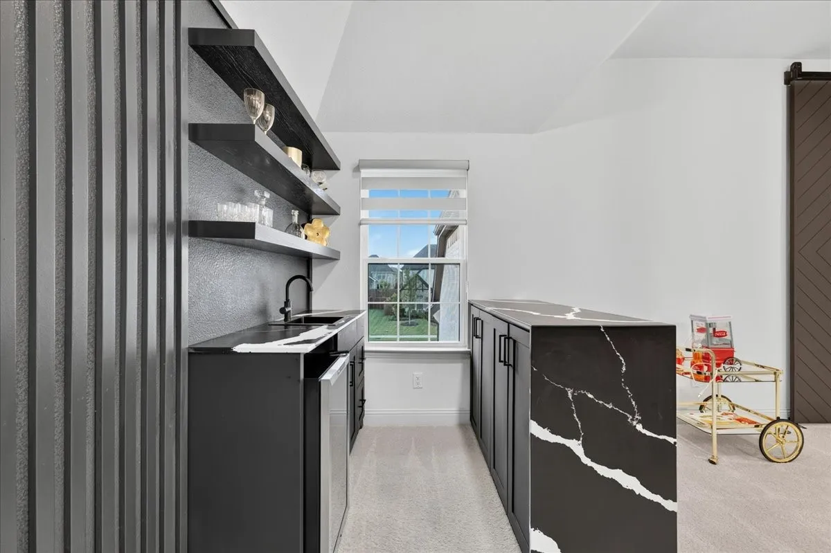 Contemporary wet bar featuring a black countertop with white veining, integrated sink, matte black faucet, and under-counter beverage refrigerator