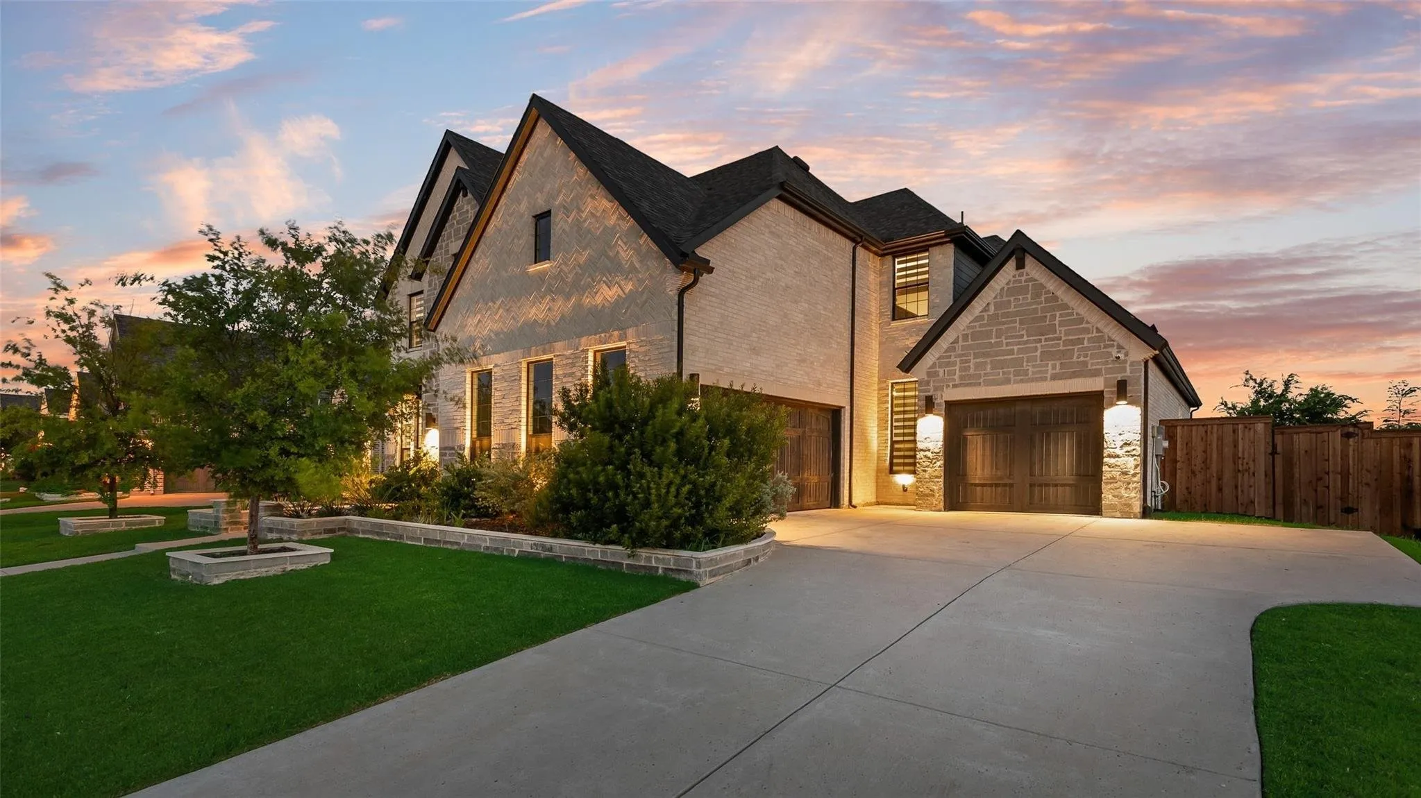 Stucco and stone exterior featuring multiple gables, a dark shingle roof, and a privacy fence