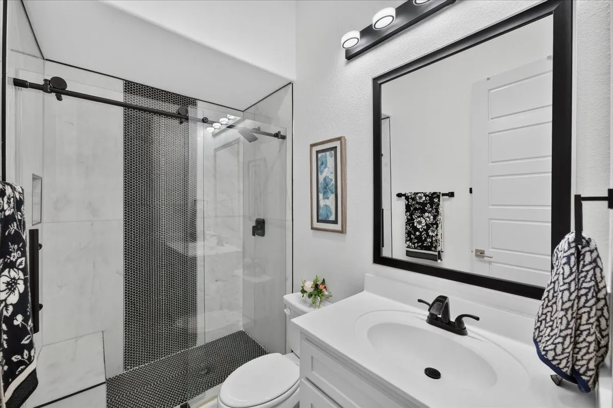 Modern bathroom featuring a glass-enclosed shower with black penny tile accent, a white vanity with integrated sink, and a framed mirror with black trim