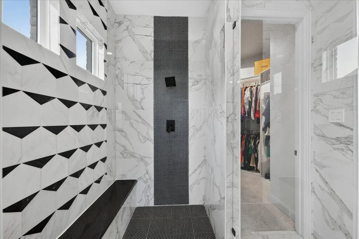 Spacious walk-in shower featuring a striking black and white geometric tile accent wall, dual matte black shower heads, and built-in bench seating