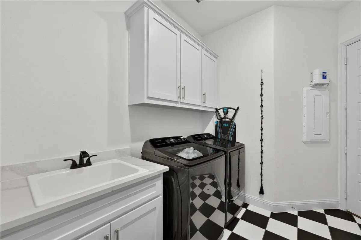 Laundry area featuring a utility sink with a matte black faucet, white shaker-style cabinetry, and striking black and white checkered flooring