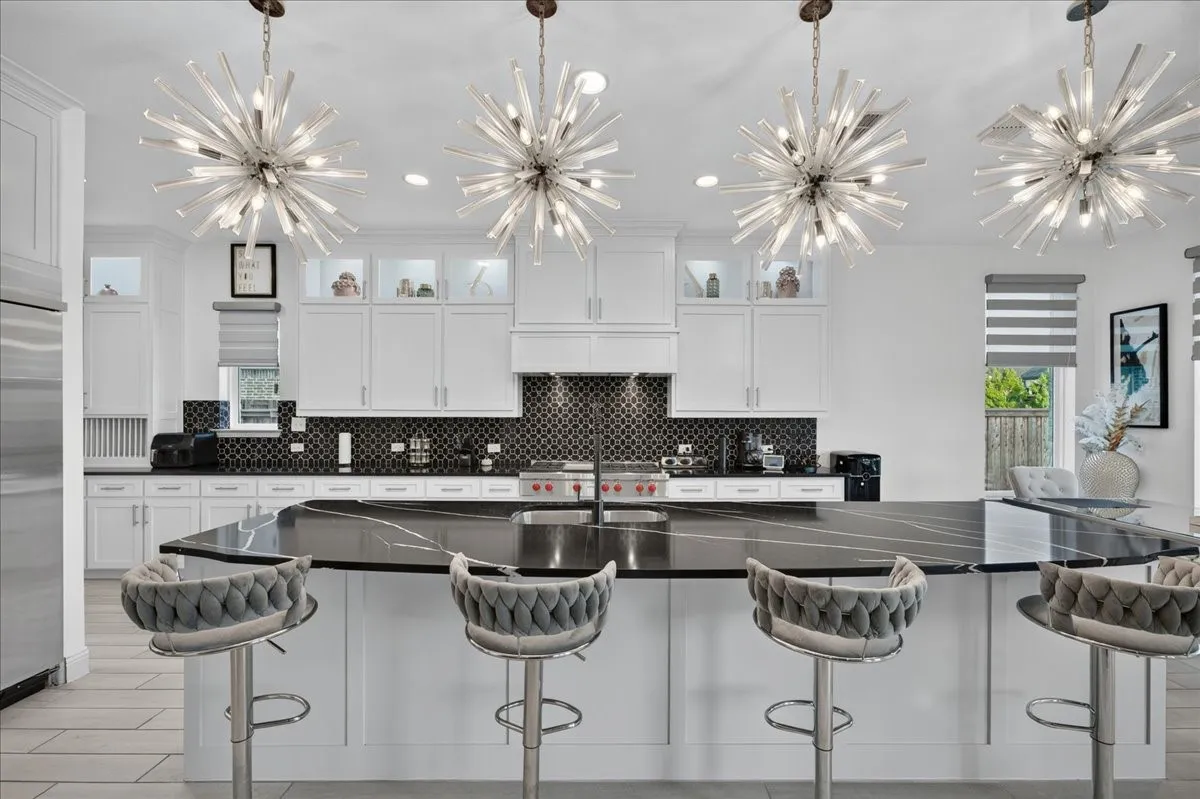 Gourmet kitchen featuring a large central island with a dark countertop, white perimeter cabinetry, a mosaic tile backsplash, and four contemporary chandeliers