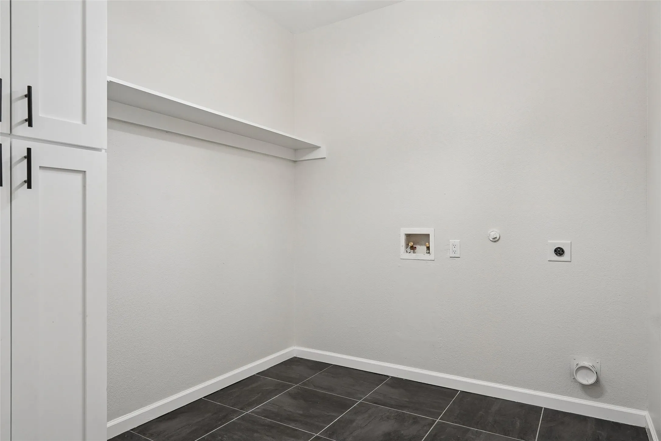 Built-in cabinetry with matte black hardware, white wall shelving, and dark tile flooring