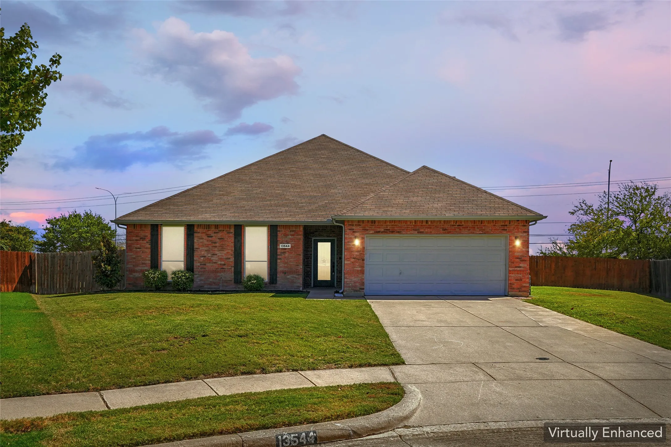 Brick exterior, attached two-car garage, concrete driveway, front lawn with mature landscaping, and privacy fencing