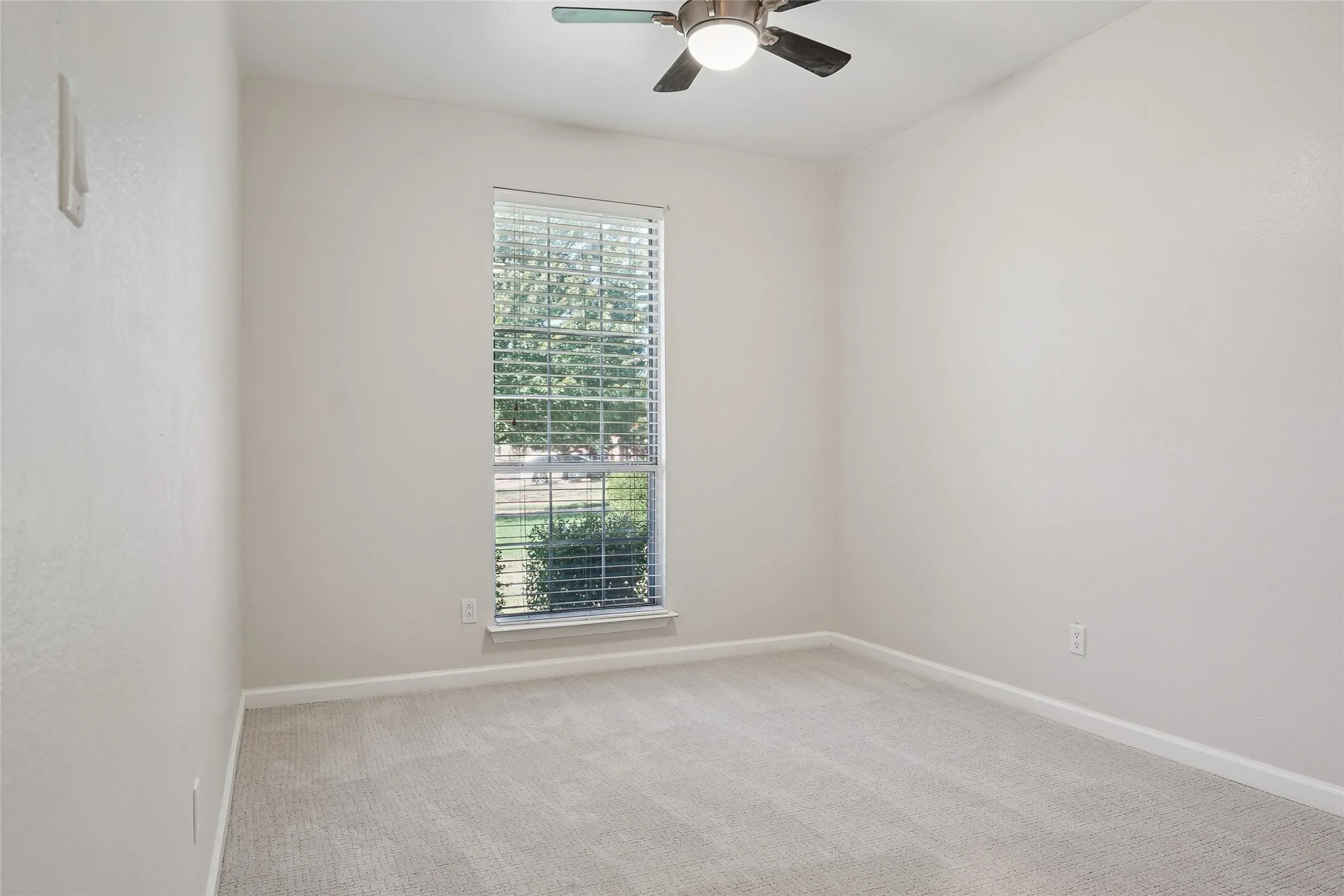 Light-toned carpeting, neutral wall color, window with horizontal blinds, and a ceiling fan with integrated lighting