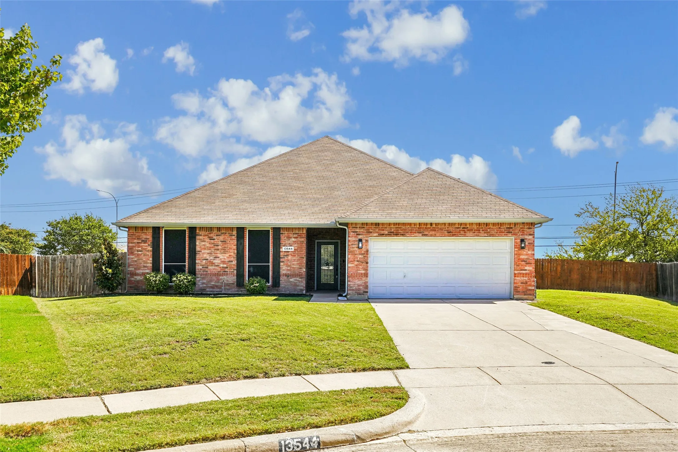 Brick exterior with dark shutters, attached two-car garage, concrete driveway, and front lawn