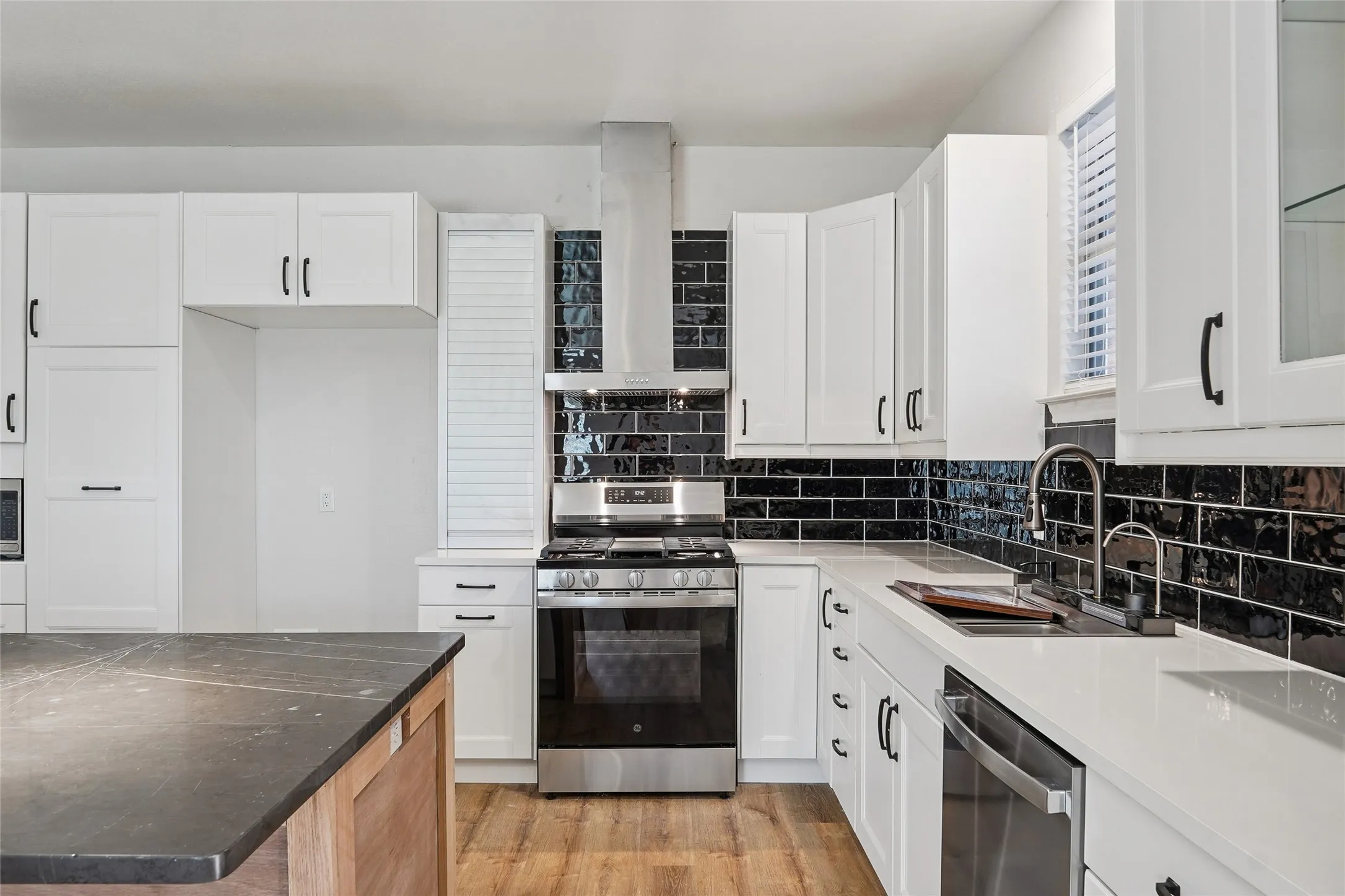 Kitchen featuring white cabinetry, black subway tile backsplash, stainless steel appliances, a kitchen island with a dark countertop, and wood-finish flooring