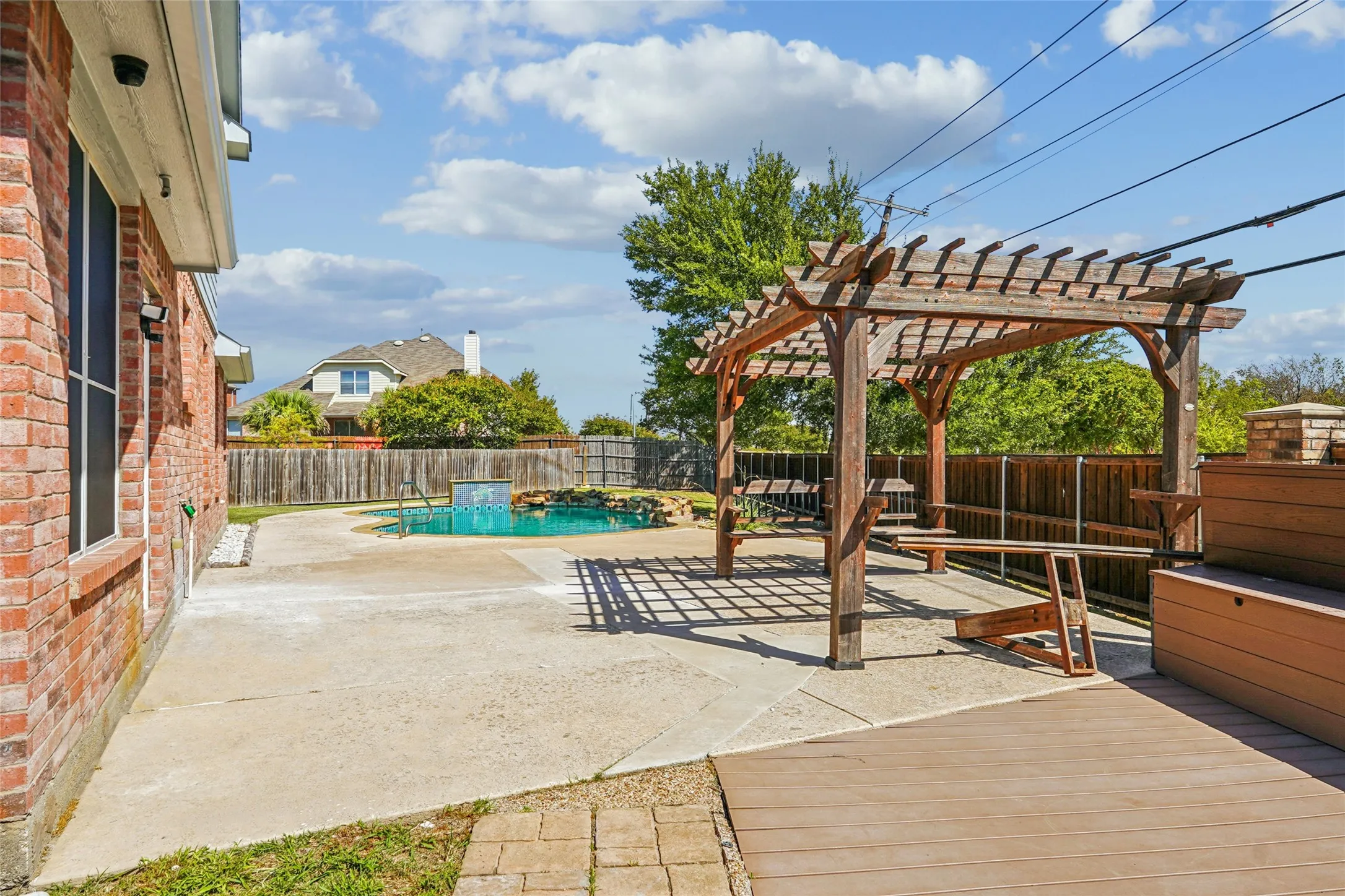 Expansive backyard featuring a swimming pool with a water feature, a wood pergola, composite decking, and a brick​​‌​​​​‌​​‌‌​‌‌​​​‌‌​‌​‌​‌​​​‌​​ exterior