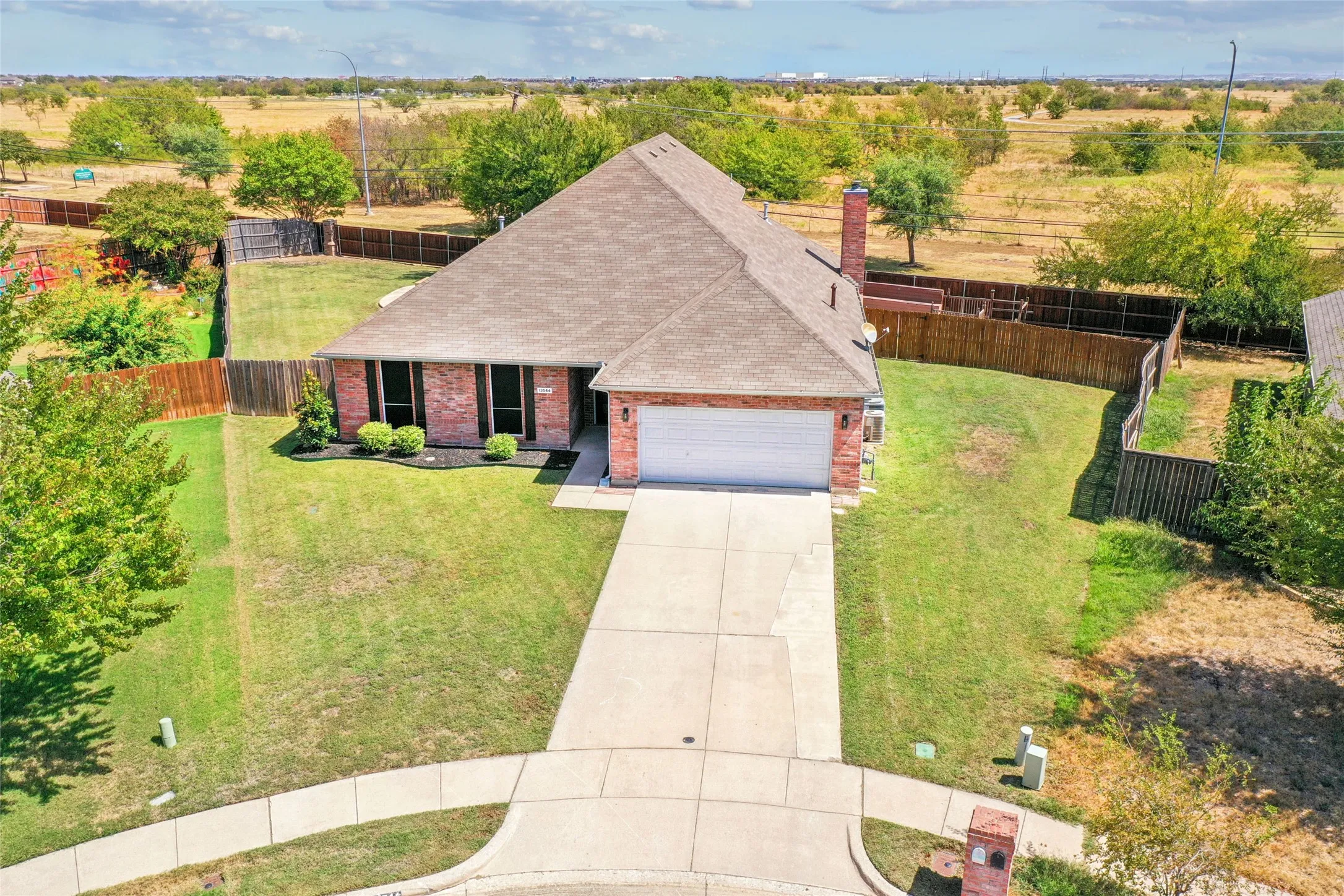 Brick exterior, attached garage, concrete driveway, fenced backyard, and mature landscaping