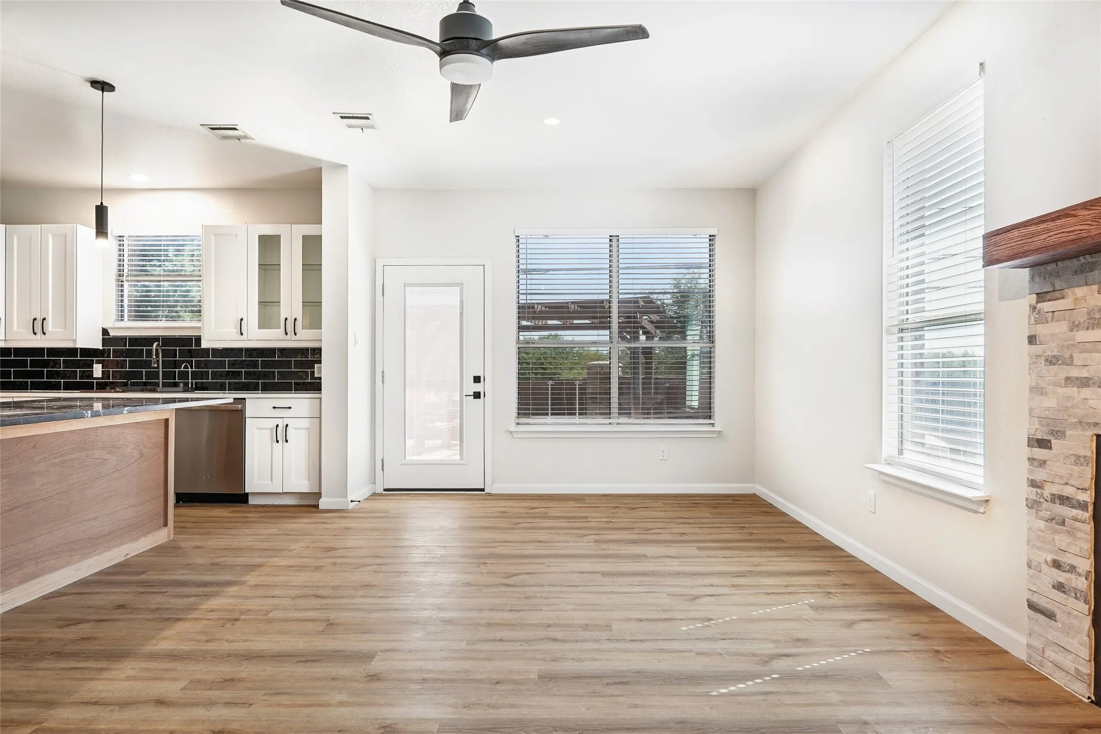 Wood-finish flooring throughout, bright white walls, modern ceiling fan, and stone-clad fireplace with a wood mantle