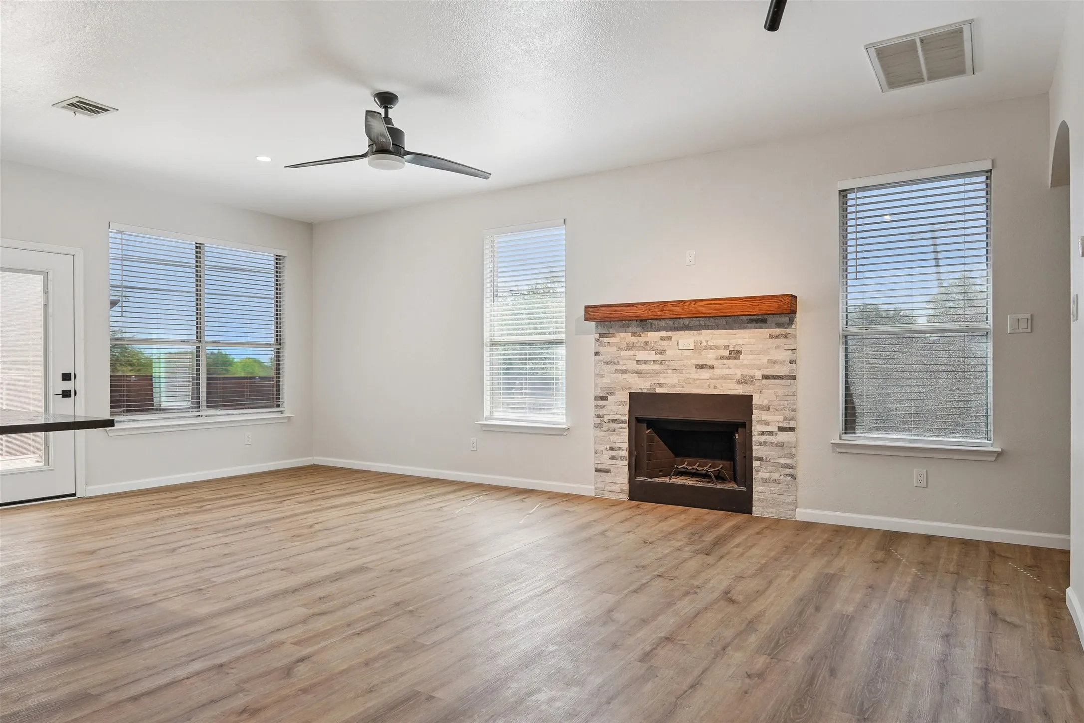 Wood-finish flooring throughout, modern ceiling fan, recessed lighting, stone-clad fireplace with wood mantle, and multiple windows