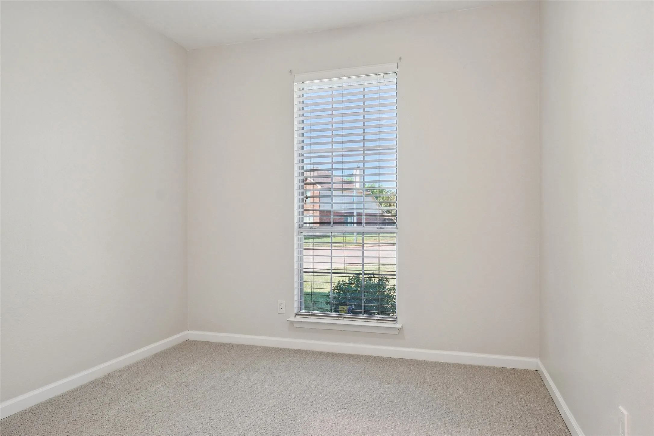 Neutral tone wall paint, carpeted flooring, and a single window with blinds
