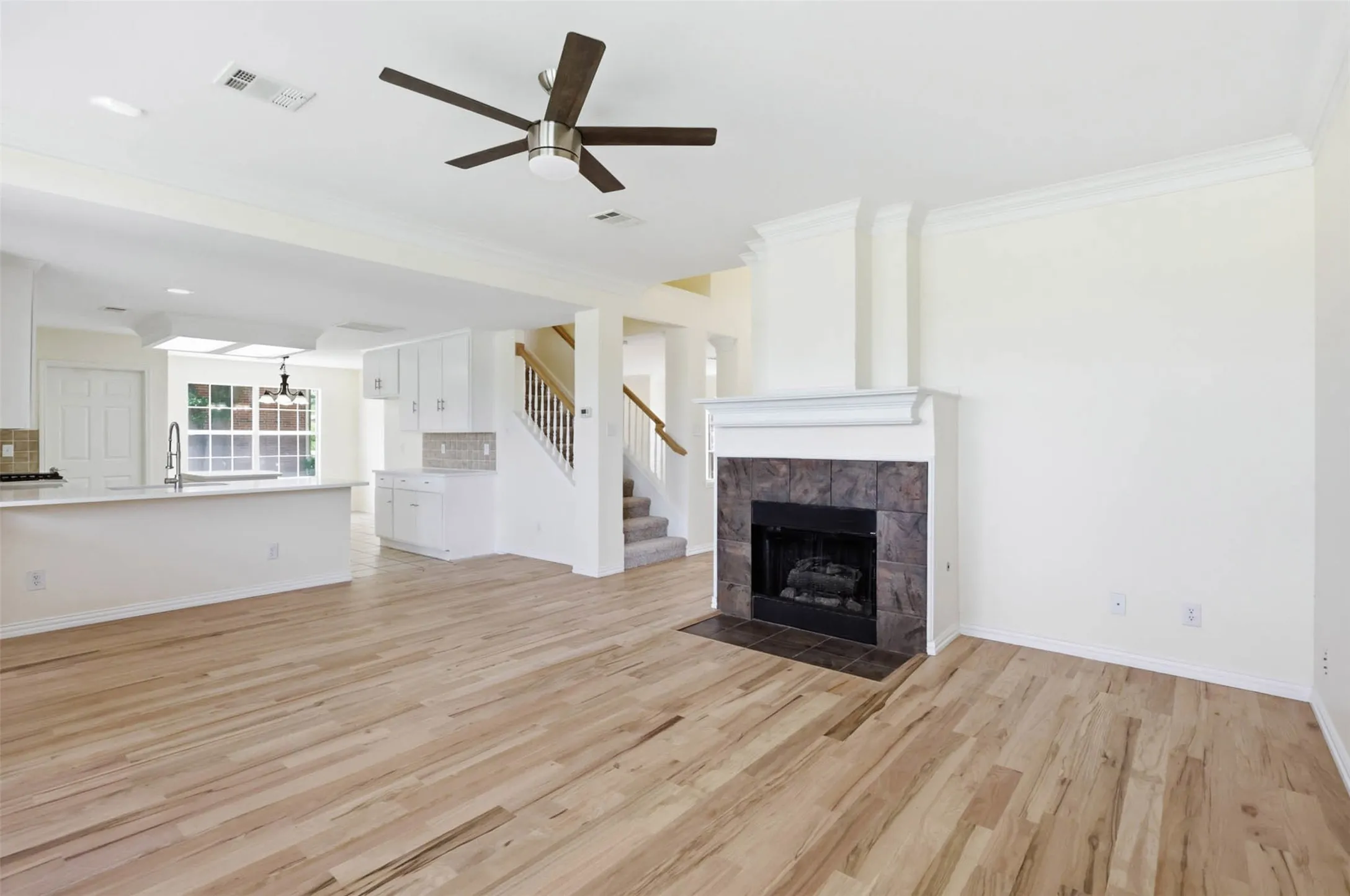 Spacious interior featuring wood-finish flooring, a contemporary ceiling fan, and a fireplace with a stone tile surround