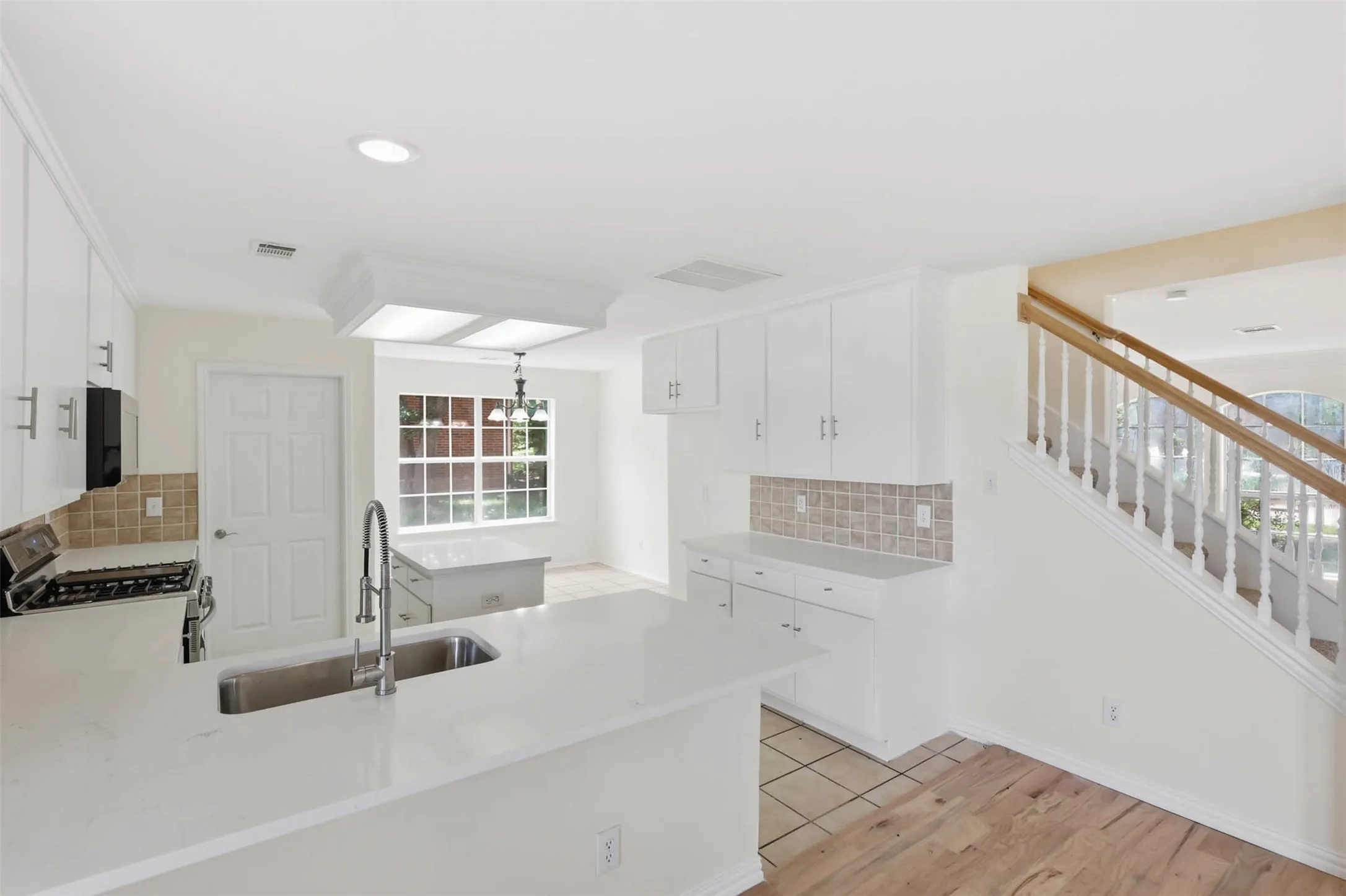 Modern kitchen with white cabinetry and light countertops, featuring a stainless steel undermount sink, built-in appliances, and a tiled backsplash