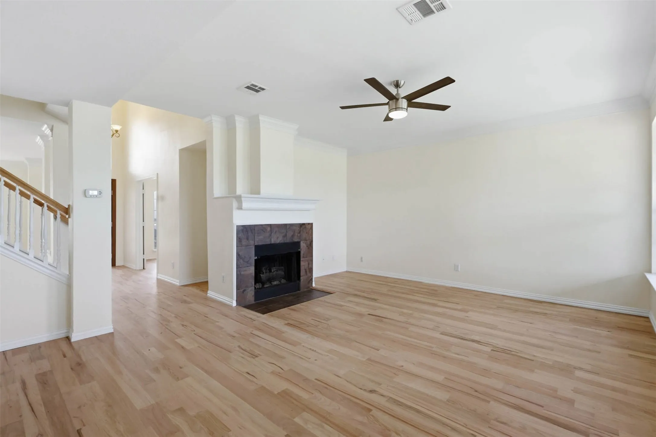 Spacious living area featuring light wood-finish flooring, a contemporary ceiling fan, and a fireplace with a tile surround and mantel