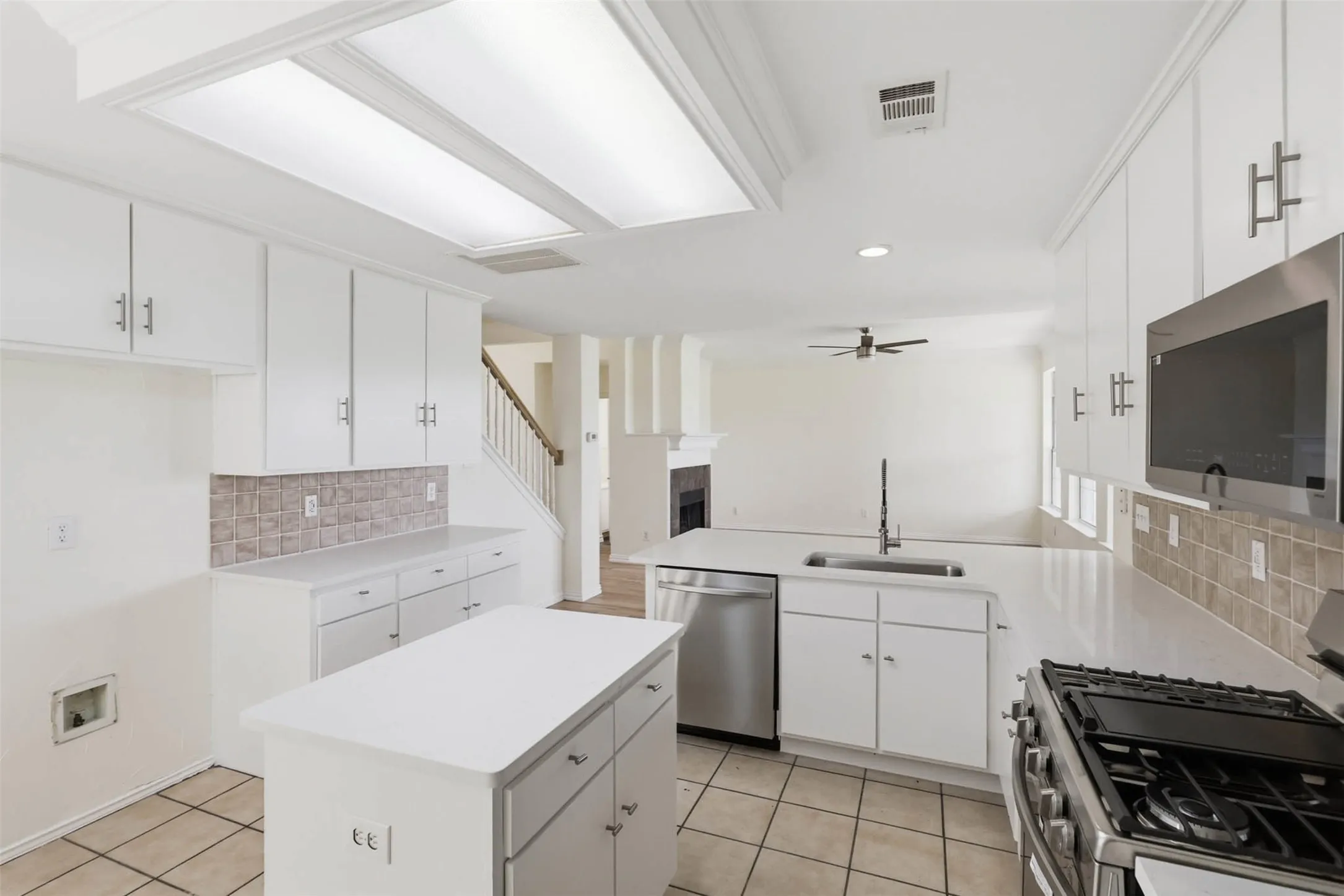 Open-concept kitchen featuring white cabinetry, light countertops, and a tiled backsplash