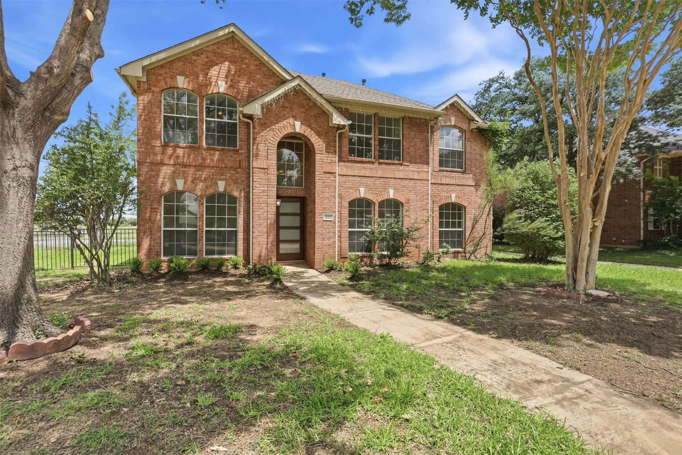 Two-story brick facade featuring an arched entryway, multiple arched and rectangular windows, a contemporary front door with horizontal lites, and a concrete pathway