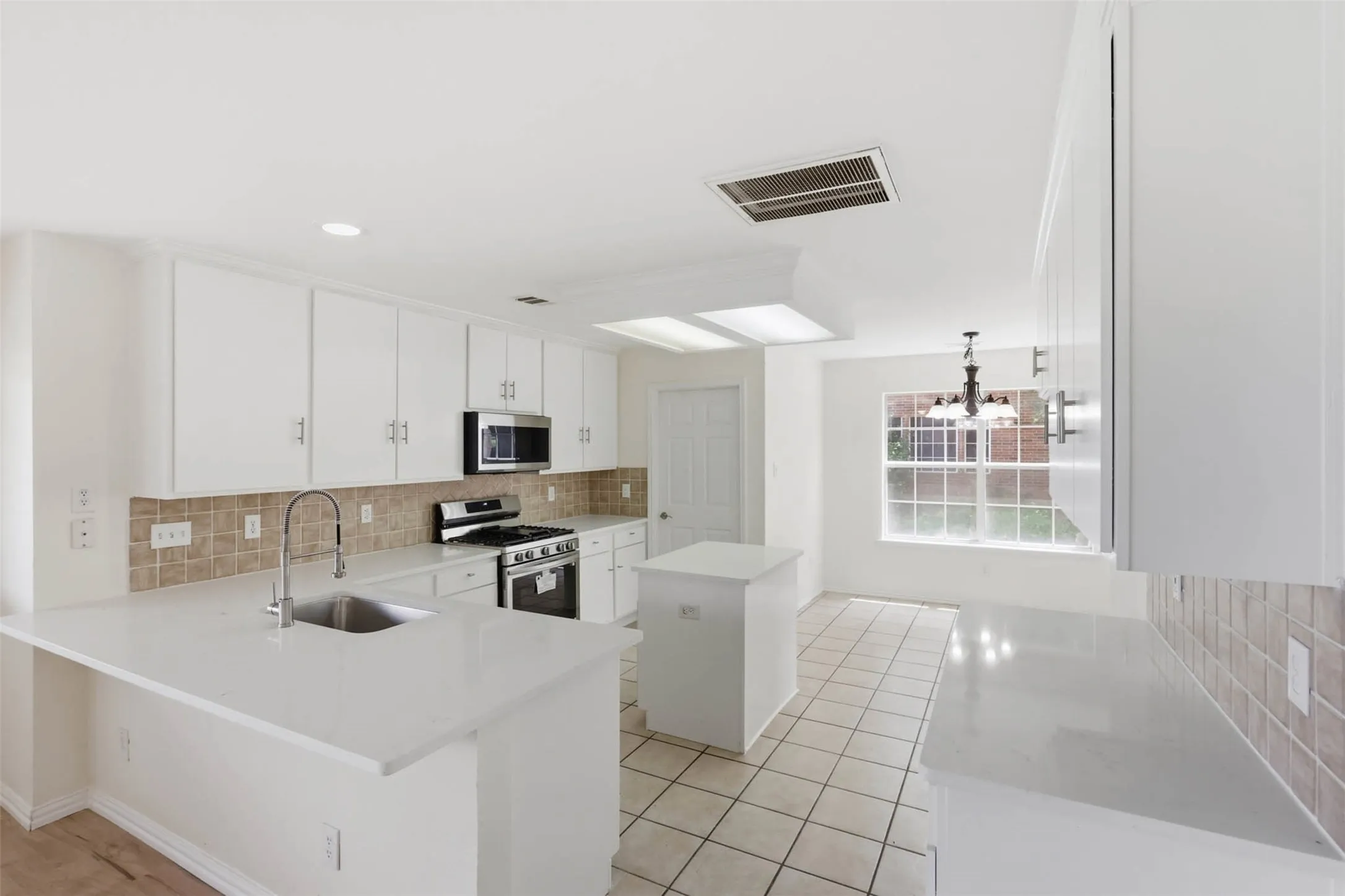 Kitchen featuring white cabinetry, light-toned countertops, a stainless steel sink with a gooseneck faucet, a tile backsplash, and stainless steel appliances