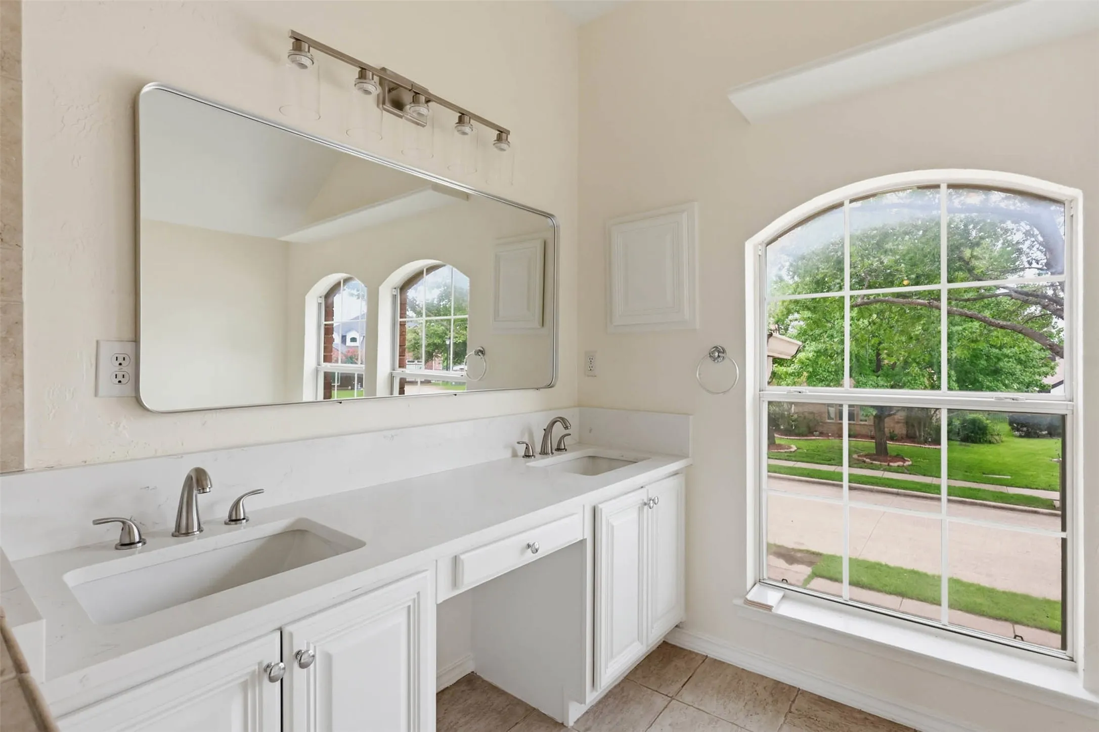 Dual vanity with integrated sinks, white cabinetry, track lighting, and an arched window