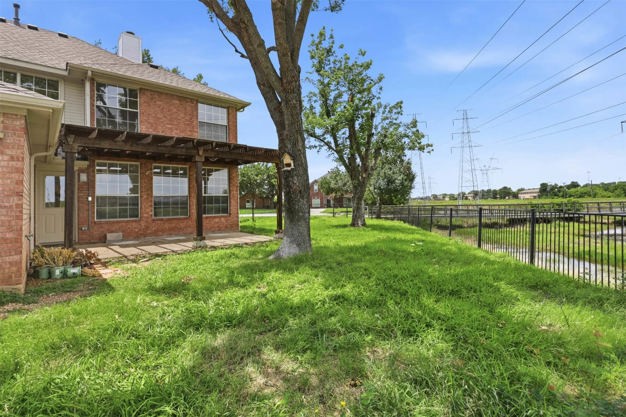 Brick exterior featuring a wooden pergola-covered patio with concrete pavers and a grassy yard