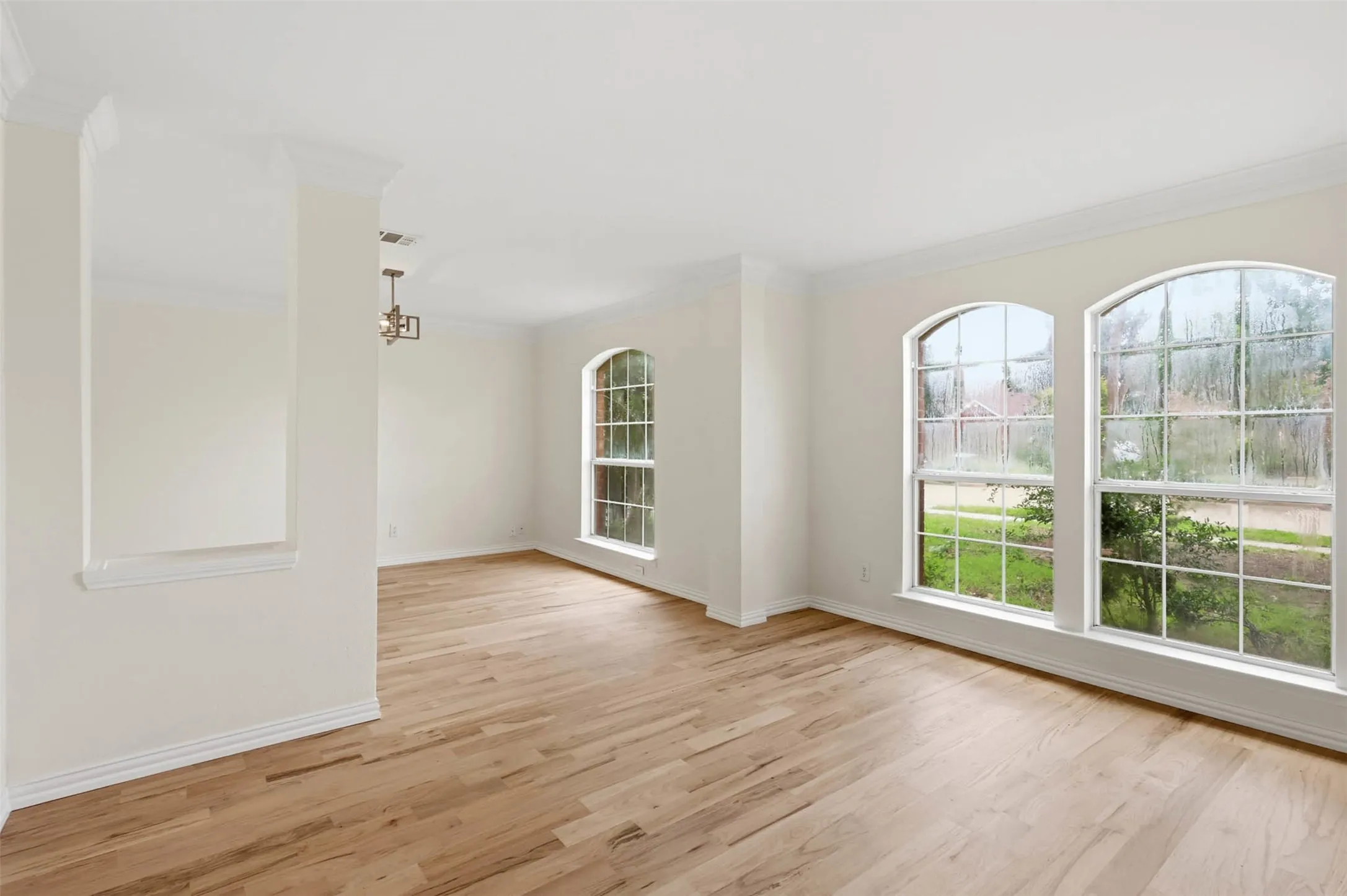 Spacious room featuring wood-finish flooring, two arched windows, crown molding, a built-in architectural wall niche, and a contemporary chandelier