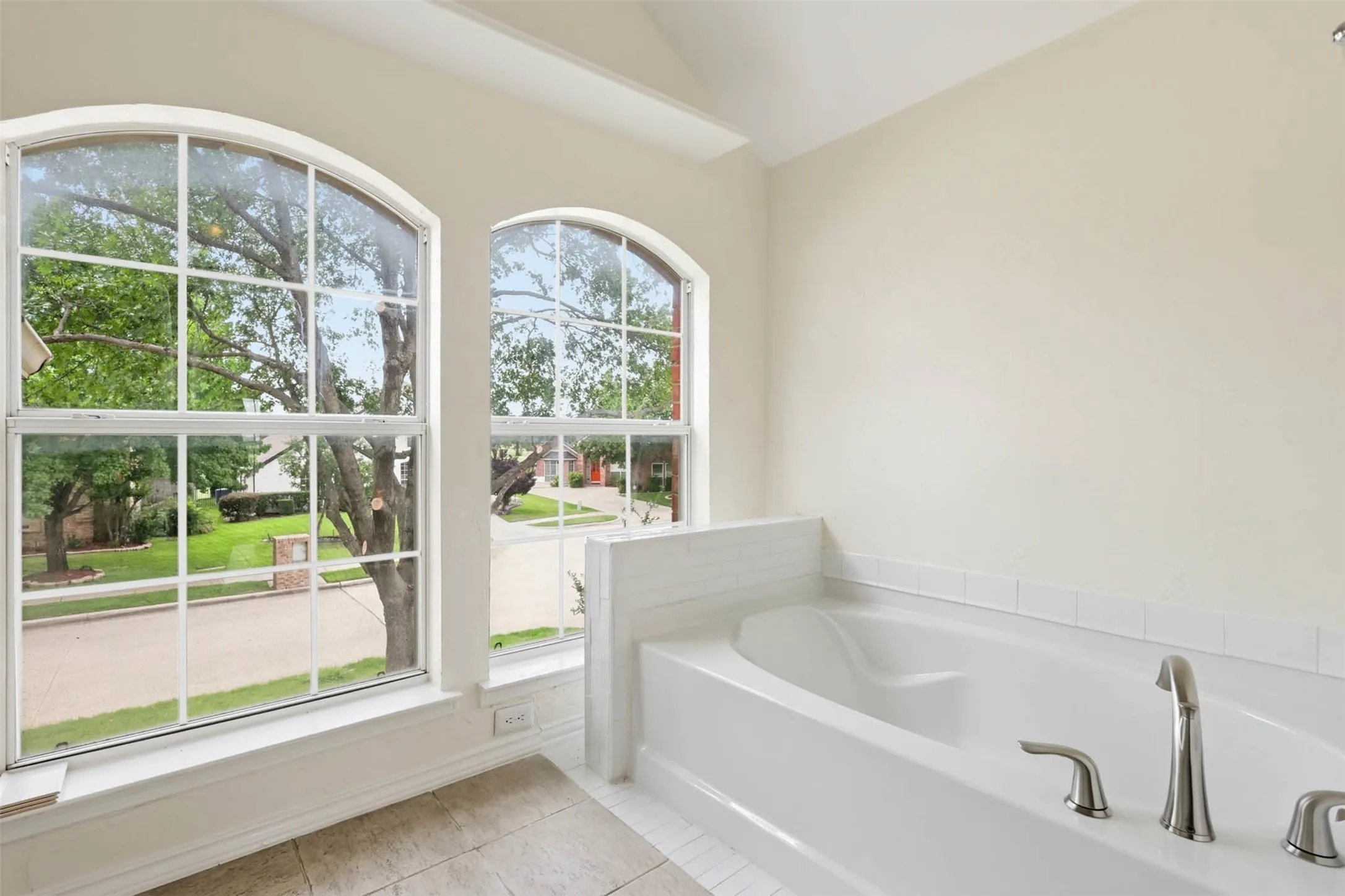 Soaking tub with chrome fixtures, surrounded by white tile and light-toned walls