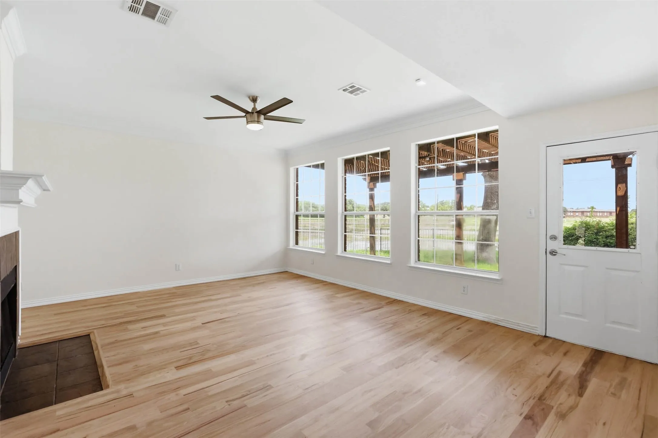 Spacious room with light wood-finish flooring, a contemporary ceiling fan, and multiple large windows