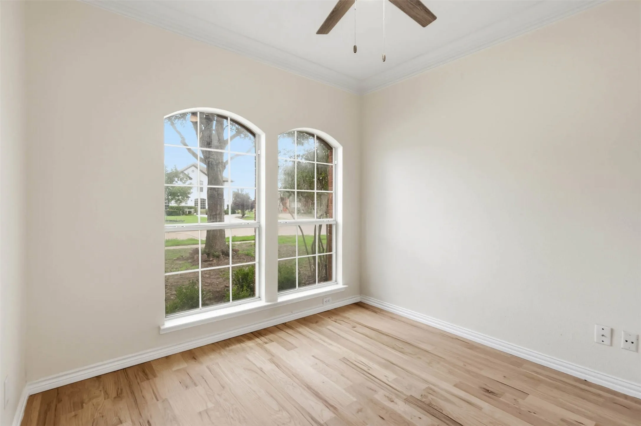 Room featuring arched windows, wood-finish flooring, a ceiling fan, crown molding, and neutral wall tones