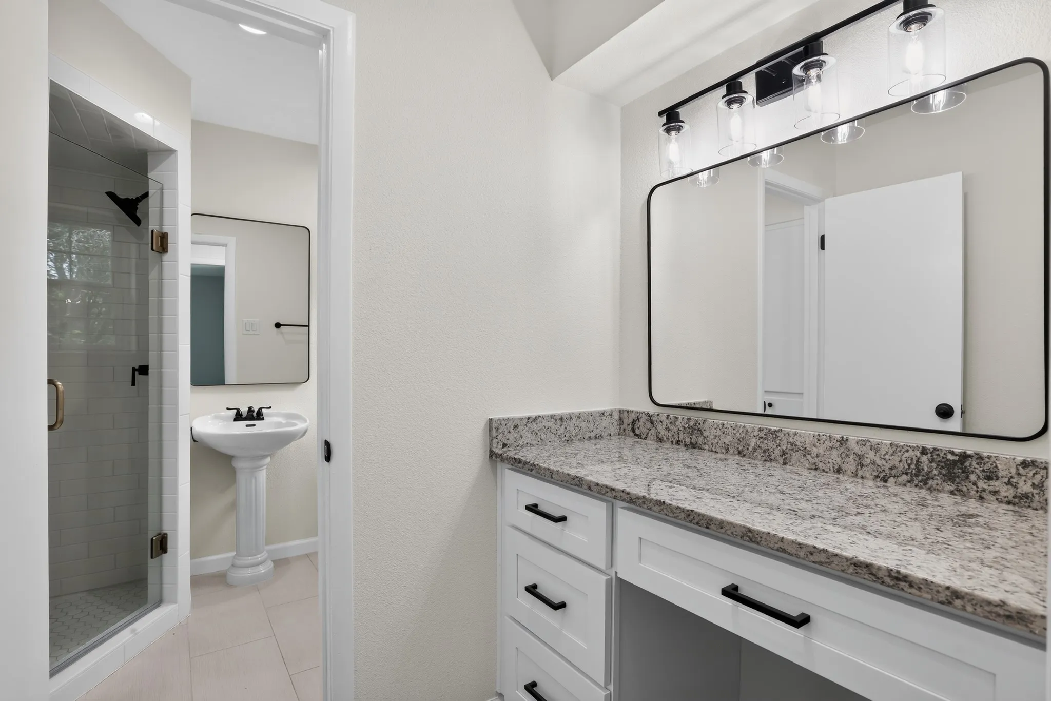 Bathroom vanity featuring a speckled countertop, a large framed mirror, and a four-light fixture