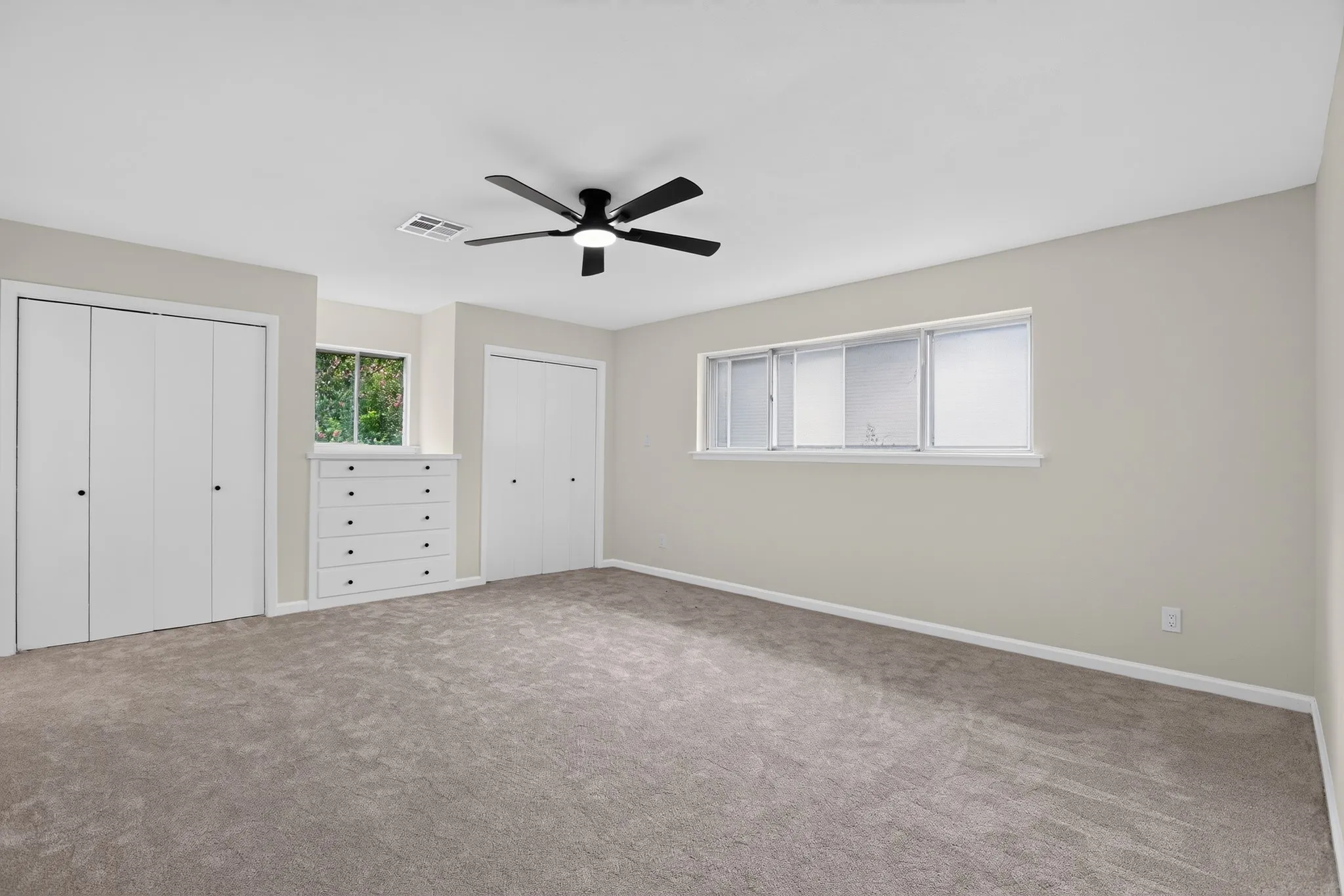 Spacious room featuring neutral carpeting, a black ceiling fan, and light-colored walls