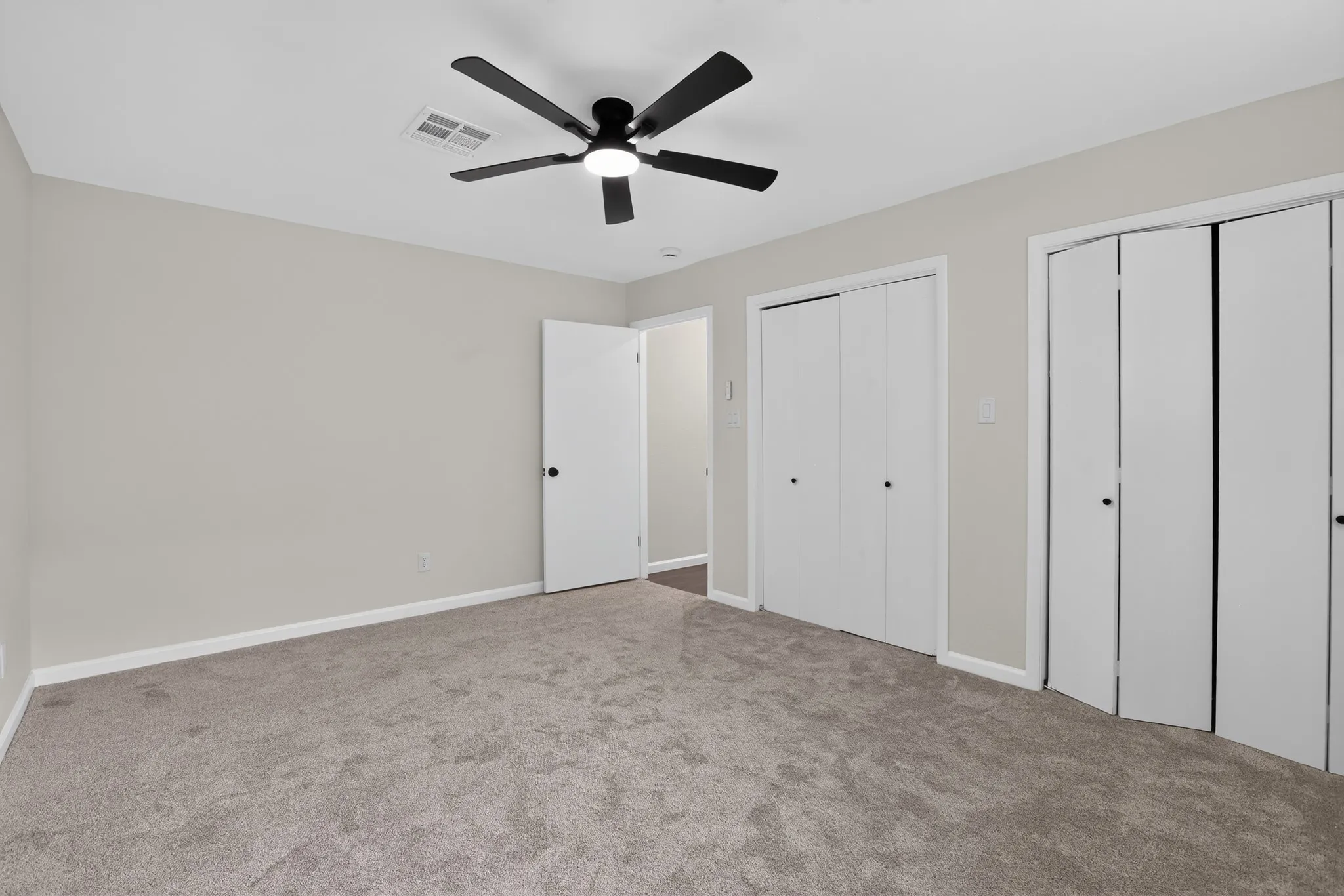 Carpeted room featuring a ceiling fan with integrated lighting, neutral wall paint, white trim, and two sets of bi-fold closet doors