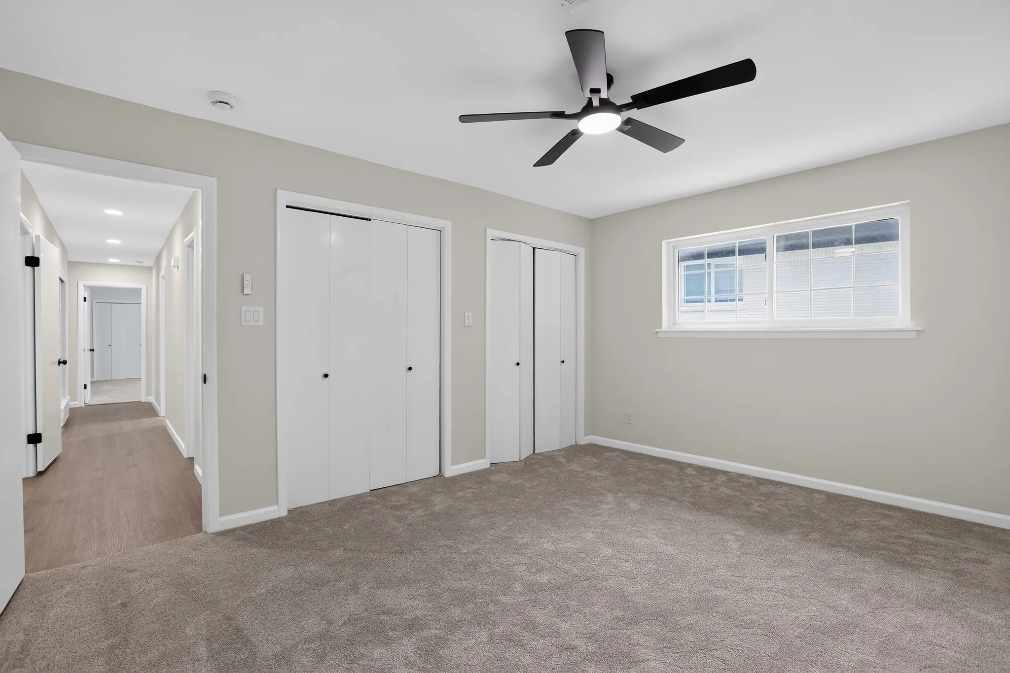 Carpeted room featuring a ceiling fan with integrated lighting, a horizontal sliding window, and two bi-fold closet doors
