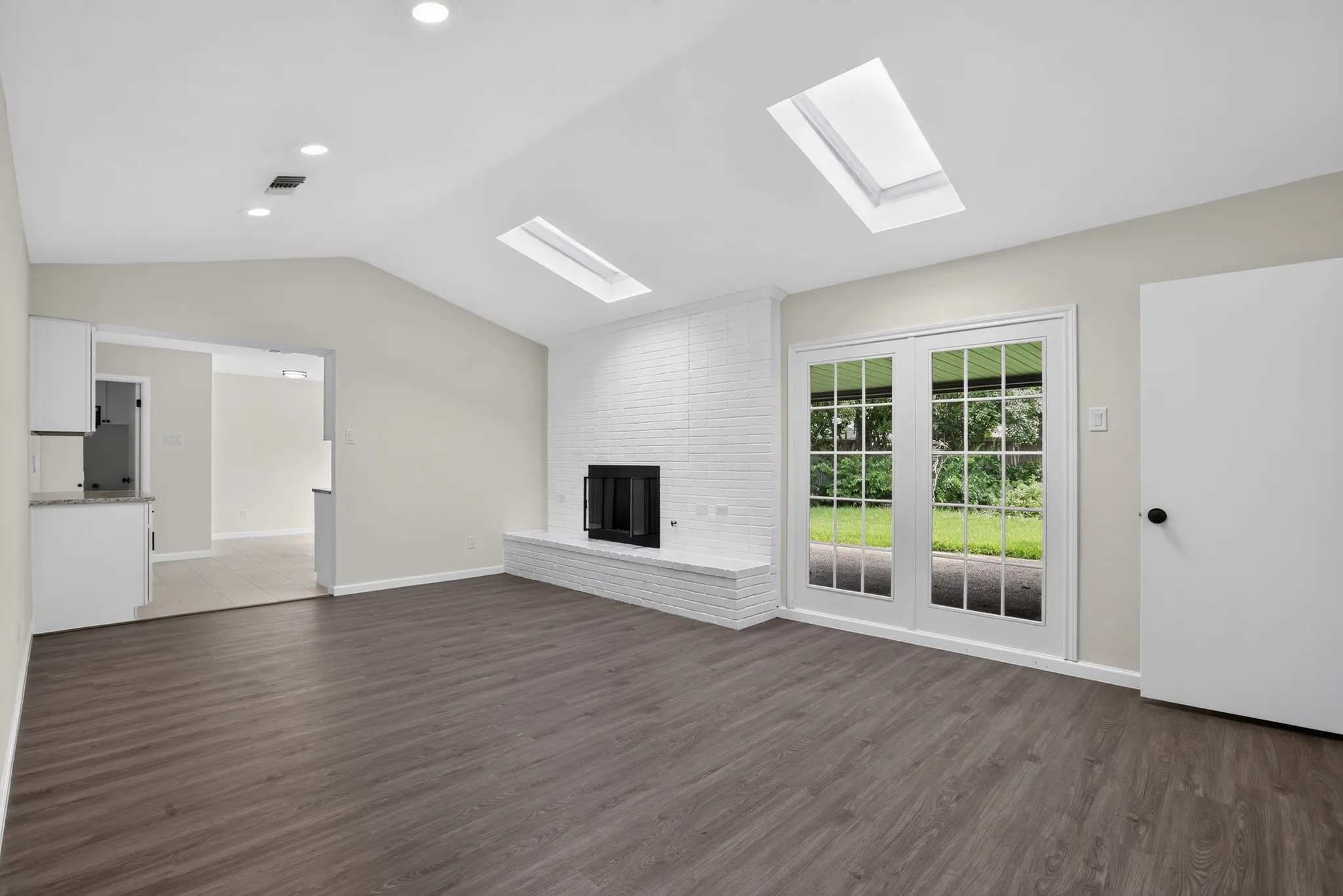 Vaulted ceiling room featuring wood-finish flooring, a white brick fireplace with a hearth, recessed lighting, and dual skylights