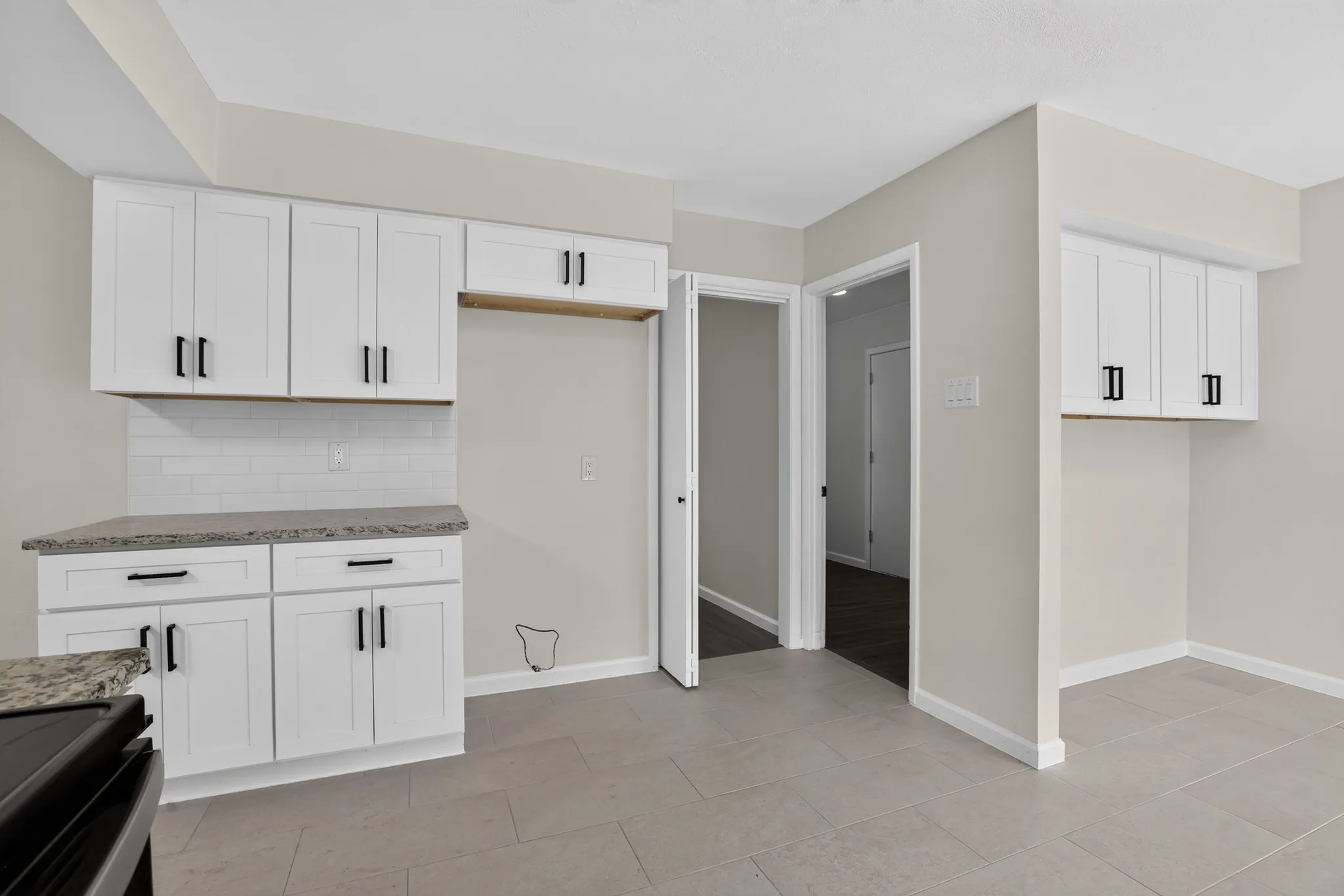 Kitchen featuring white shaker-style cabinetry, dark hardware, light gray countertops, and a white subway tile backsplash