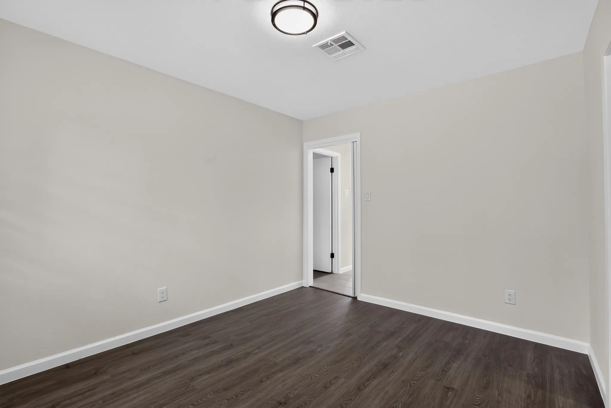 Interior room featuring dark wood-finish flooring, light neutral wall paint, and white baseboards