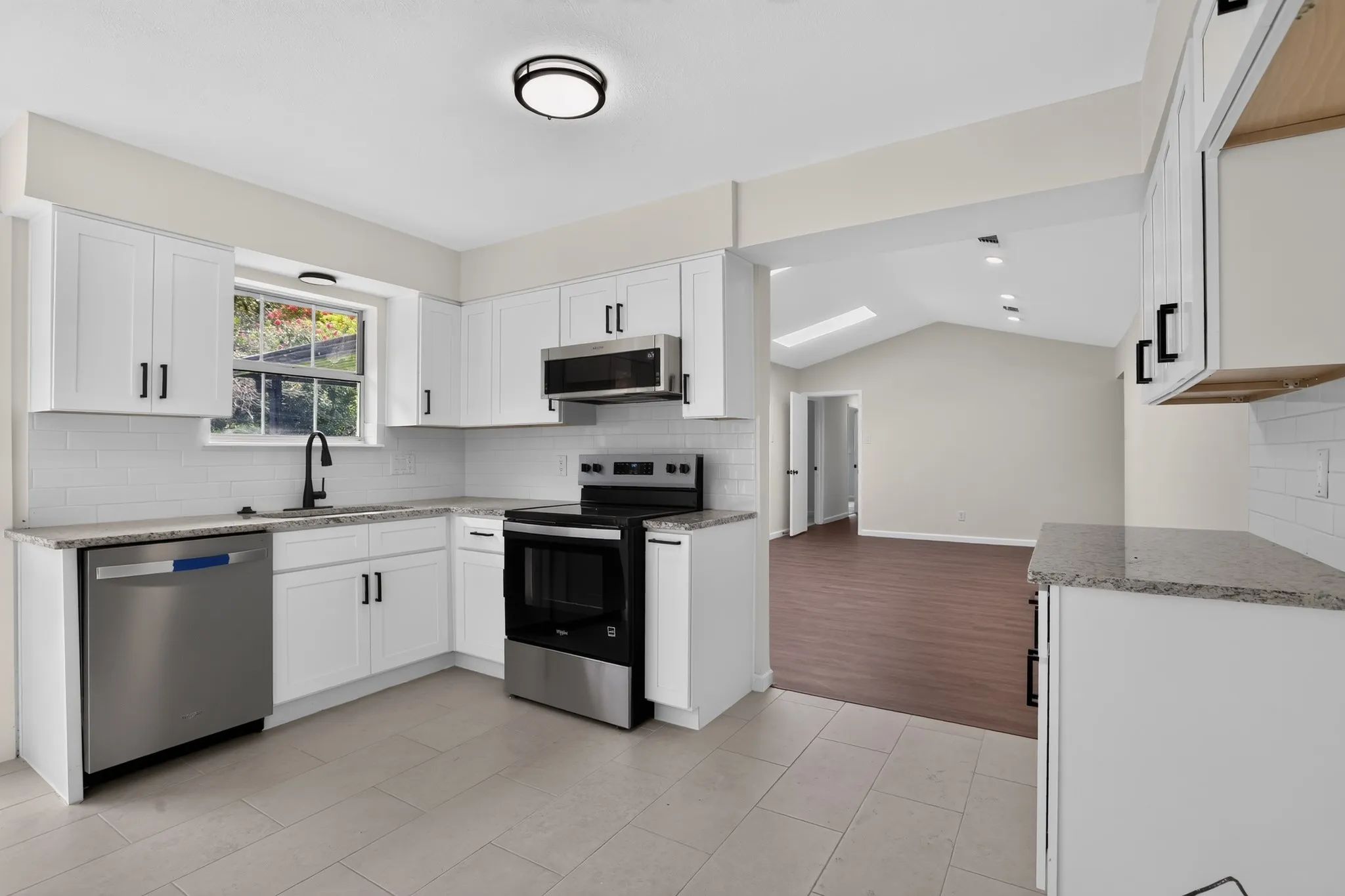 Bright kitchen featuring white shaker cabinetry, stainless steel appliances, granite-style countertops, a subway tile backsplash, and light-toned tile flooring