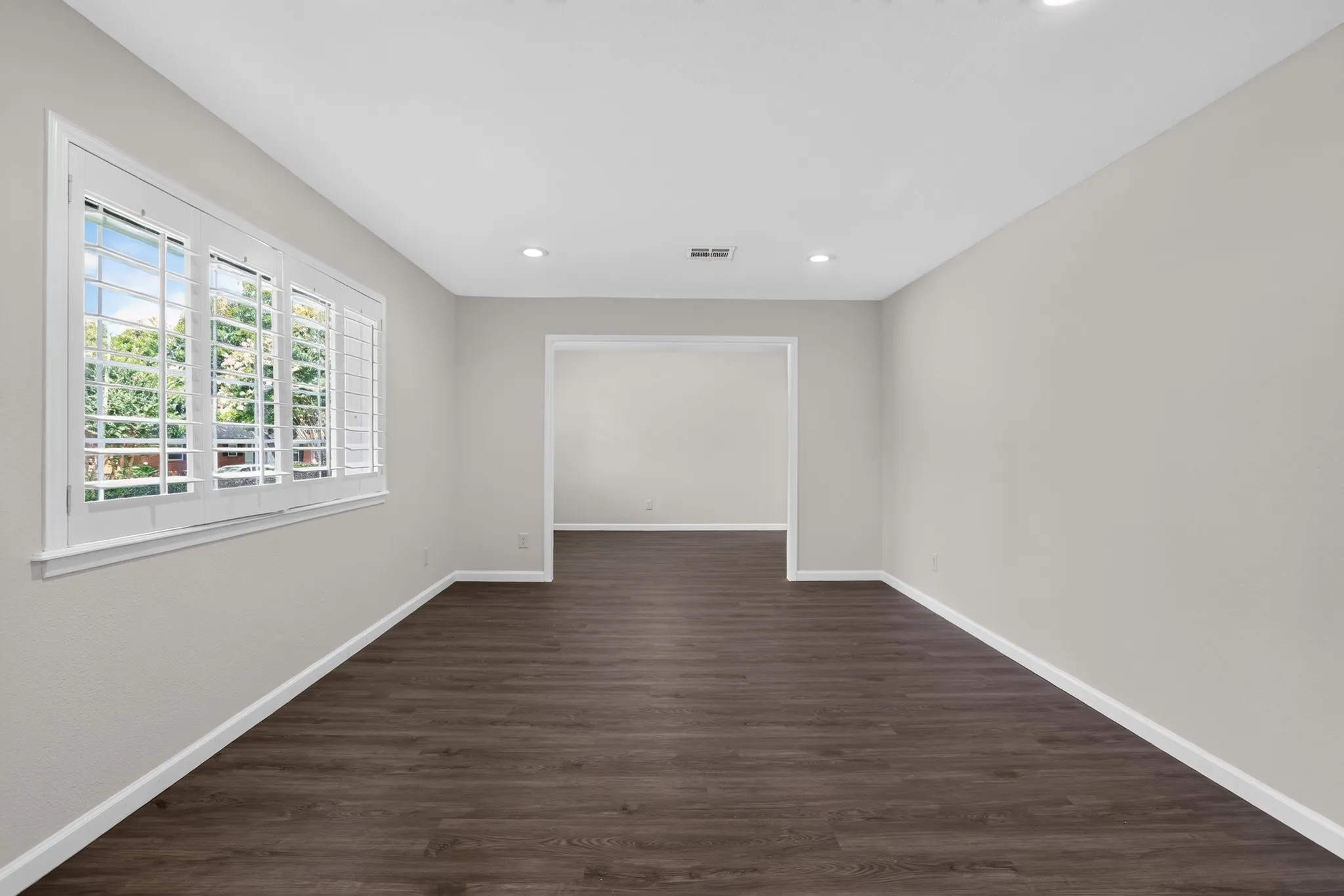 Spacious room featuring dark wood-finish flooring, light neutral-toned walls, and recessed lighting