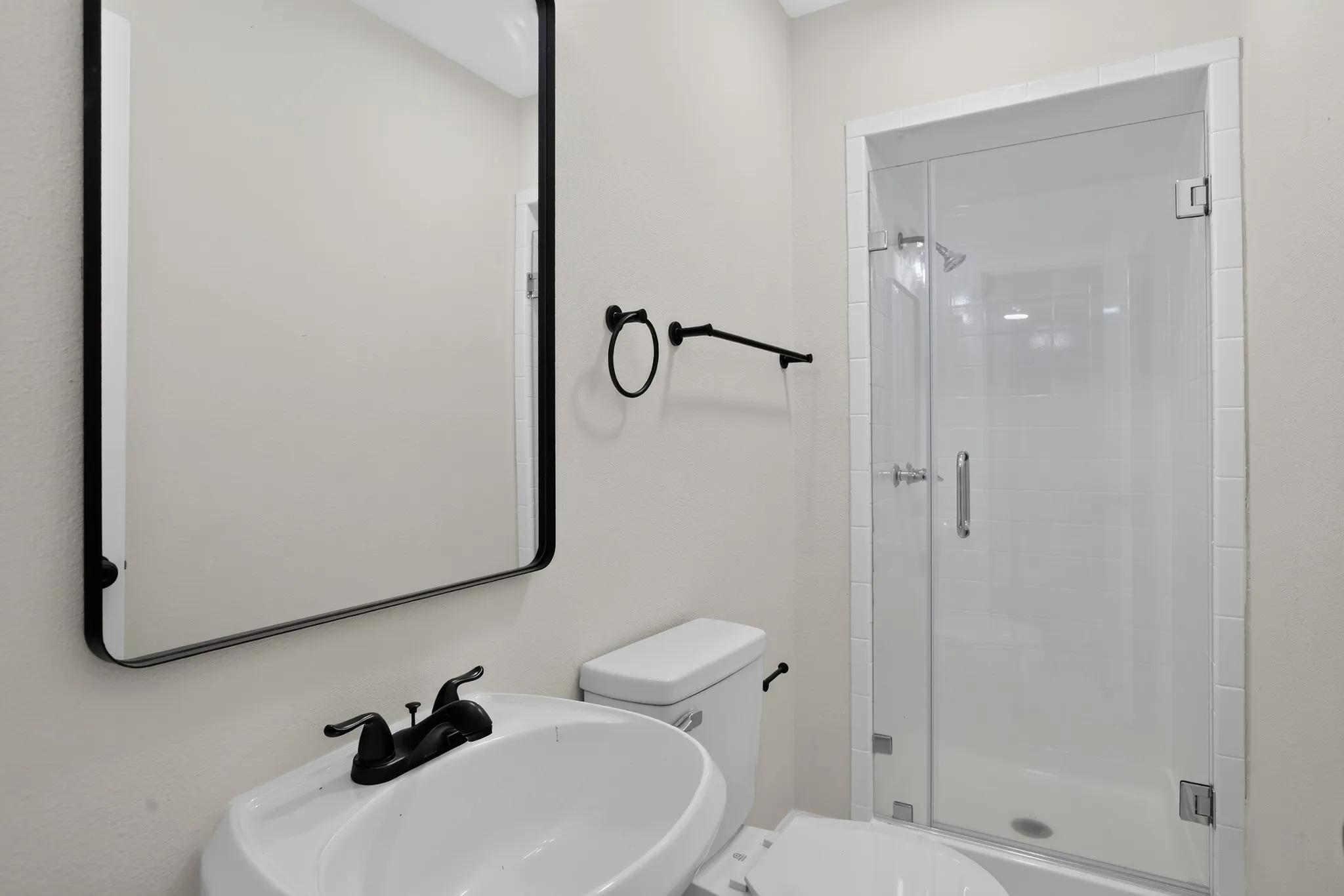 Full bathroom featuring a frameless glass shower enclosure, white pedestal sink with matte black faucet, and a rectangular mirror with a black frame