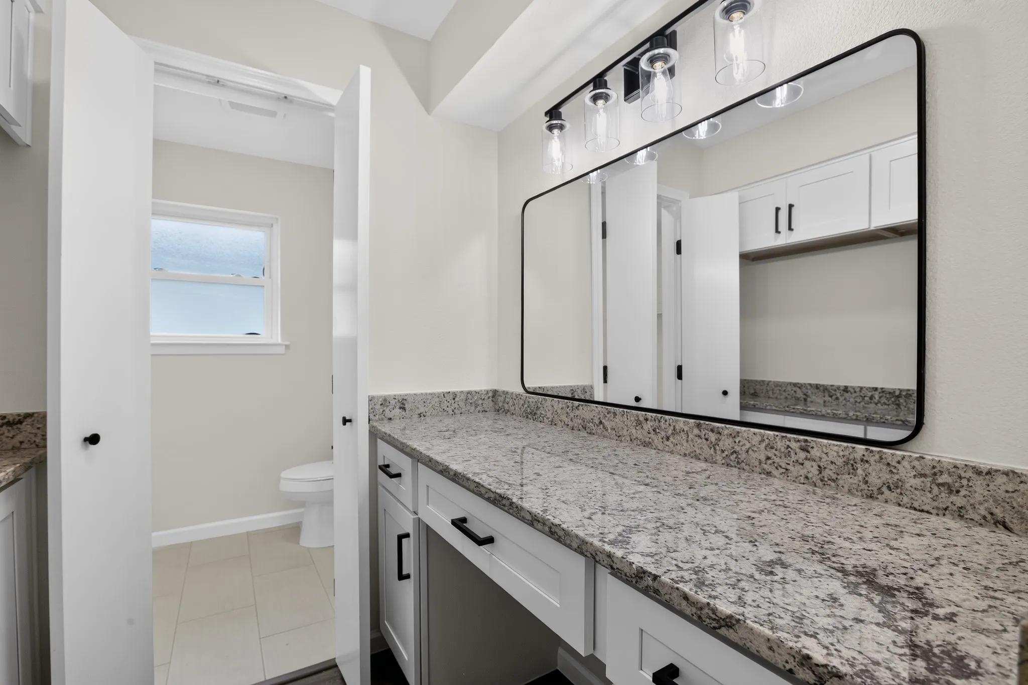 Vanity area featuring a spacious stone countertop, white cabinetry with black hardware, a rectangular mirror with a black frame, and a multi-light fixture