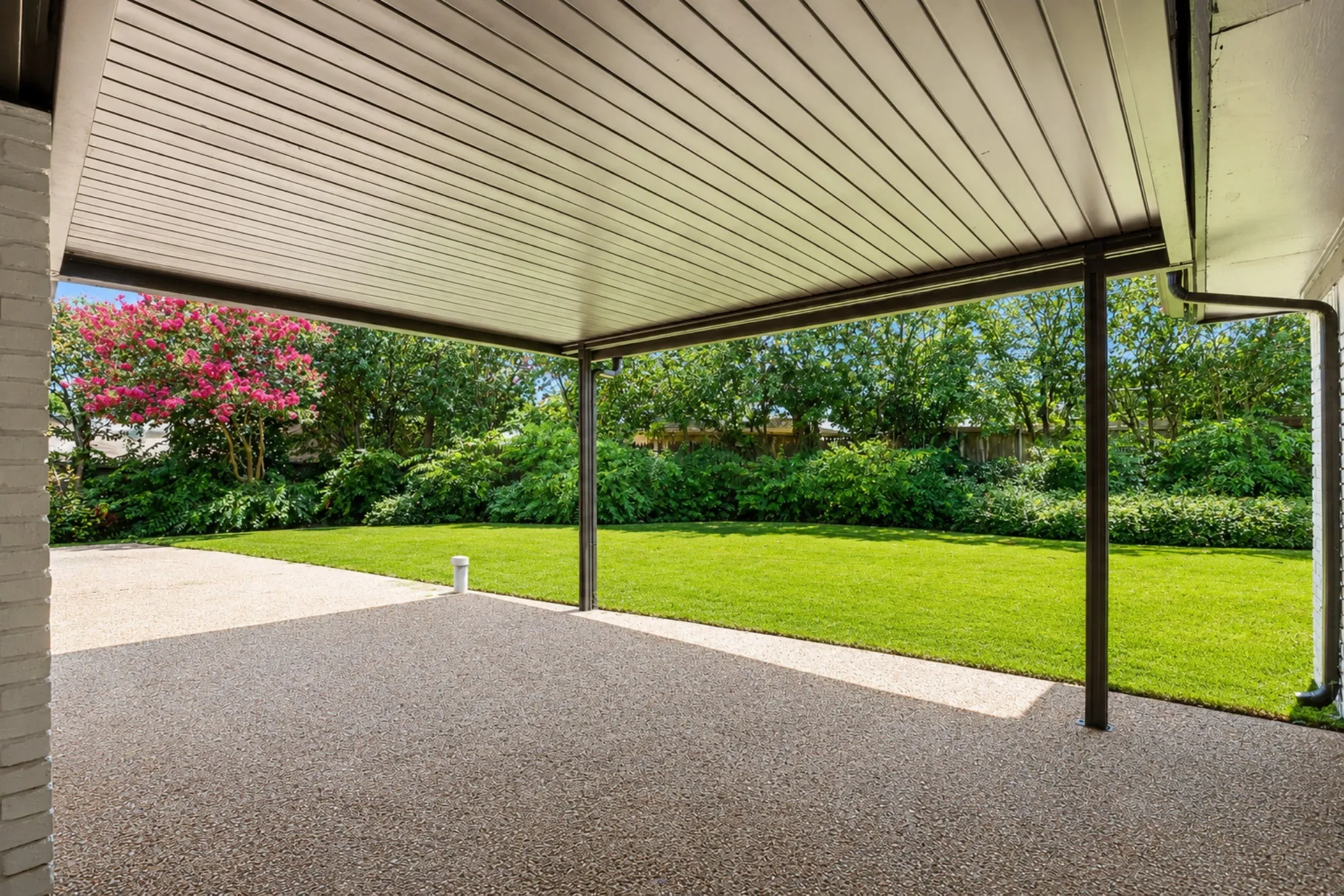 Covered patio featuring an exposed aggregate surface, a slatted ceiling, and black support columns