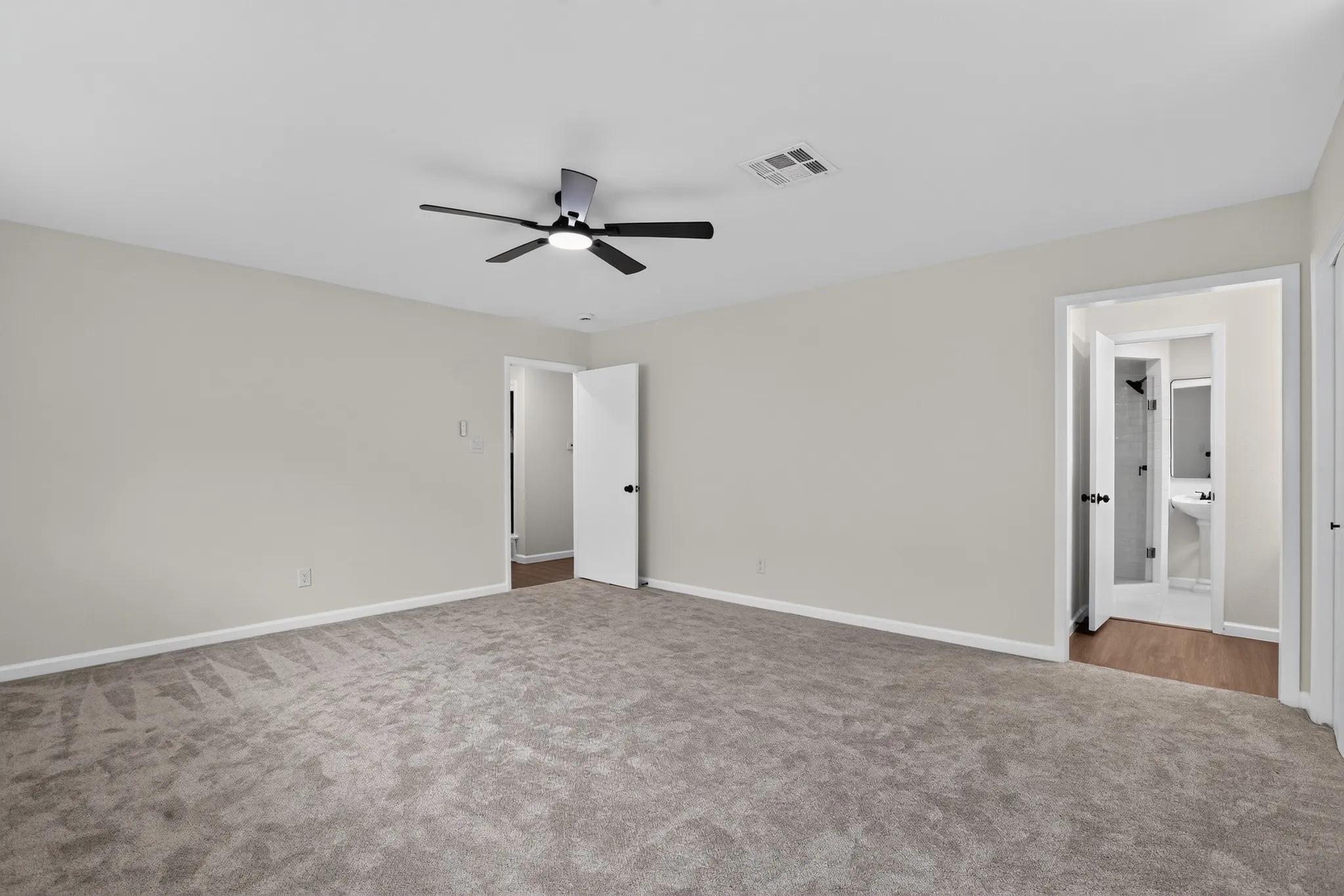 Spacious room featuring neutral carpet flooring, light-toned walls, and a modern ceiling fan with integrated lighting