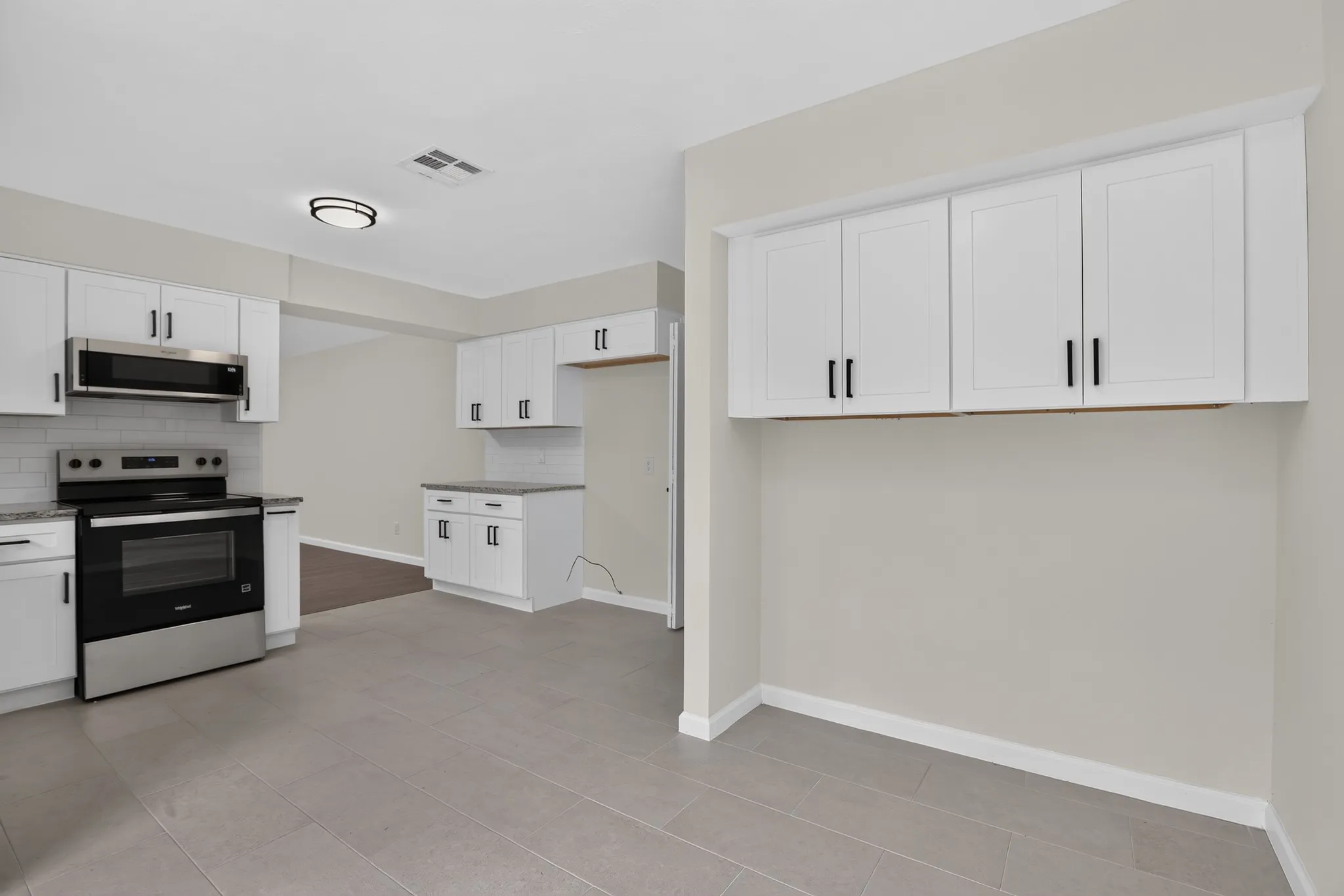 Modern kitchen featuring white shaker cabinetry with black hardware, stainless steel appliances, subway tile backsplash, and light-toned flooring