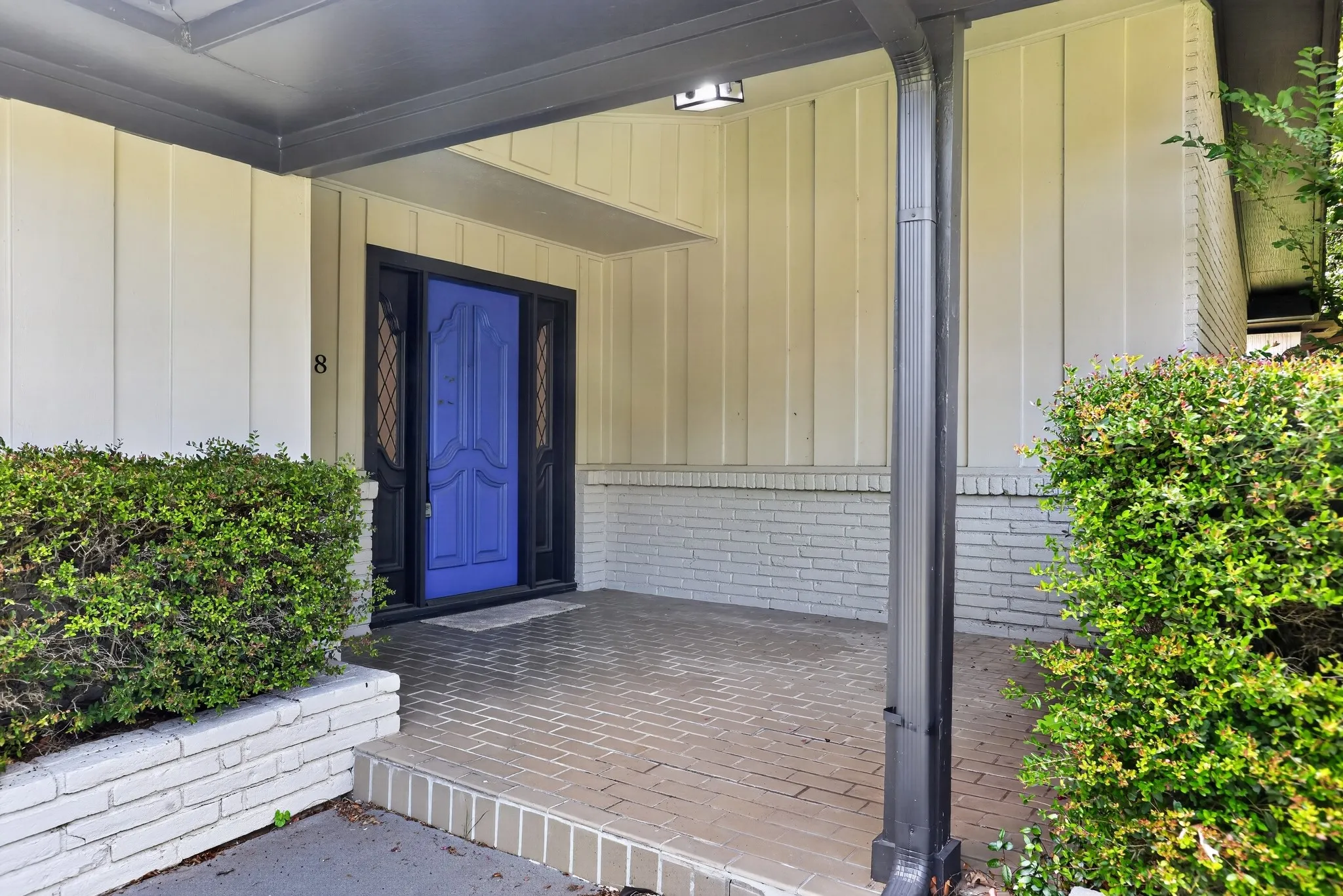 Covered entry featuring a vibrant blue front door with decorative glass side panels, board and batten siding, painted brick details, and a brick paver porch