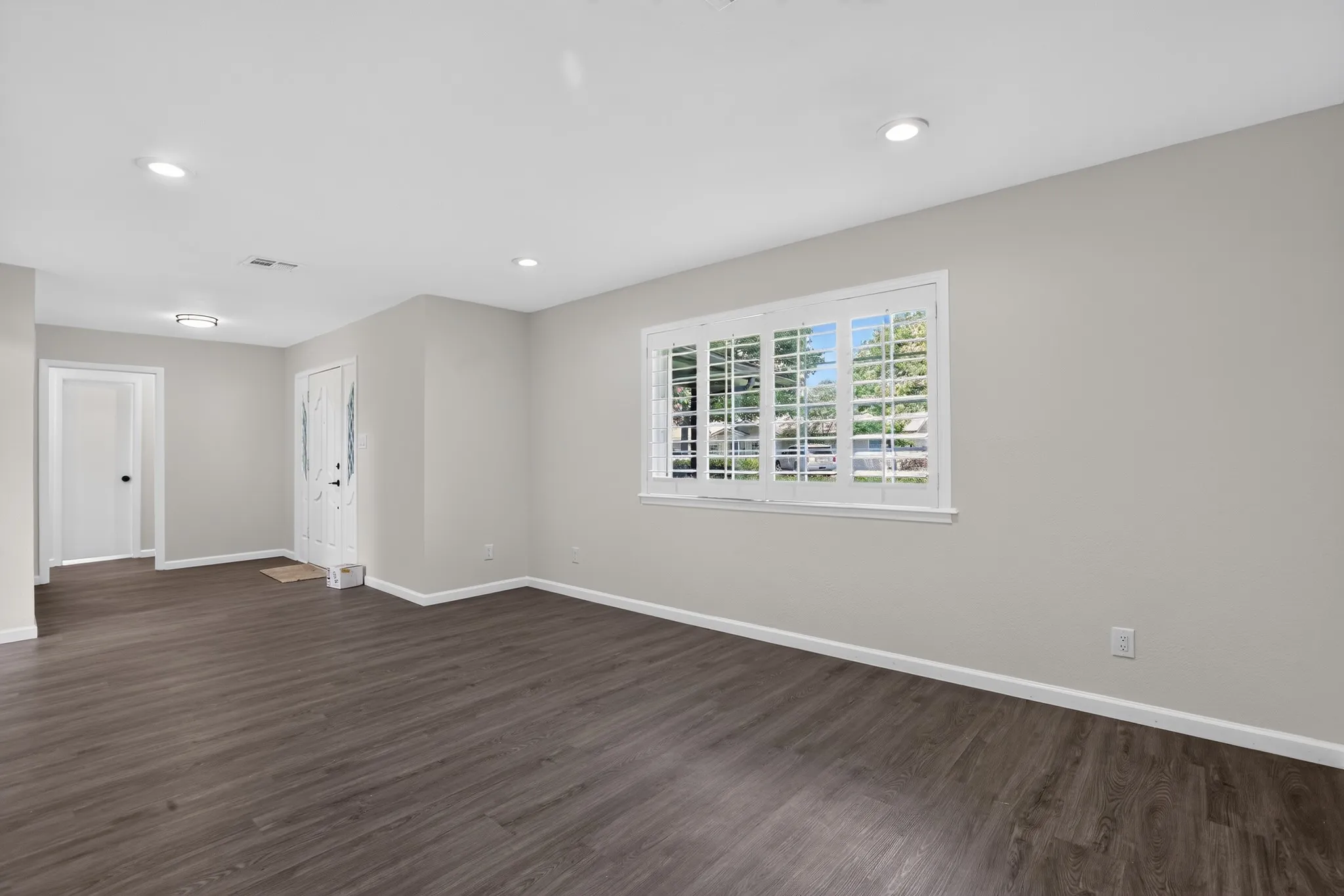 Spacious room featuring wood-finish flooring, recessed lighting, and a window with plantation shutters