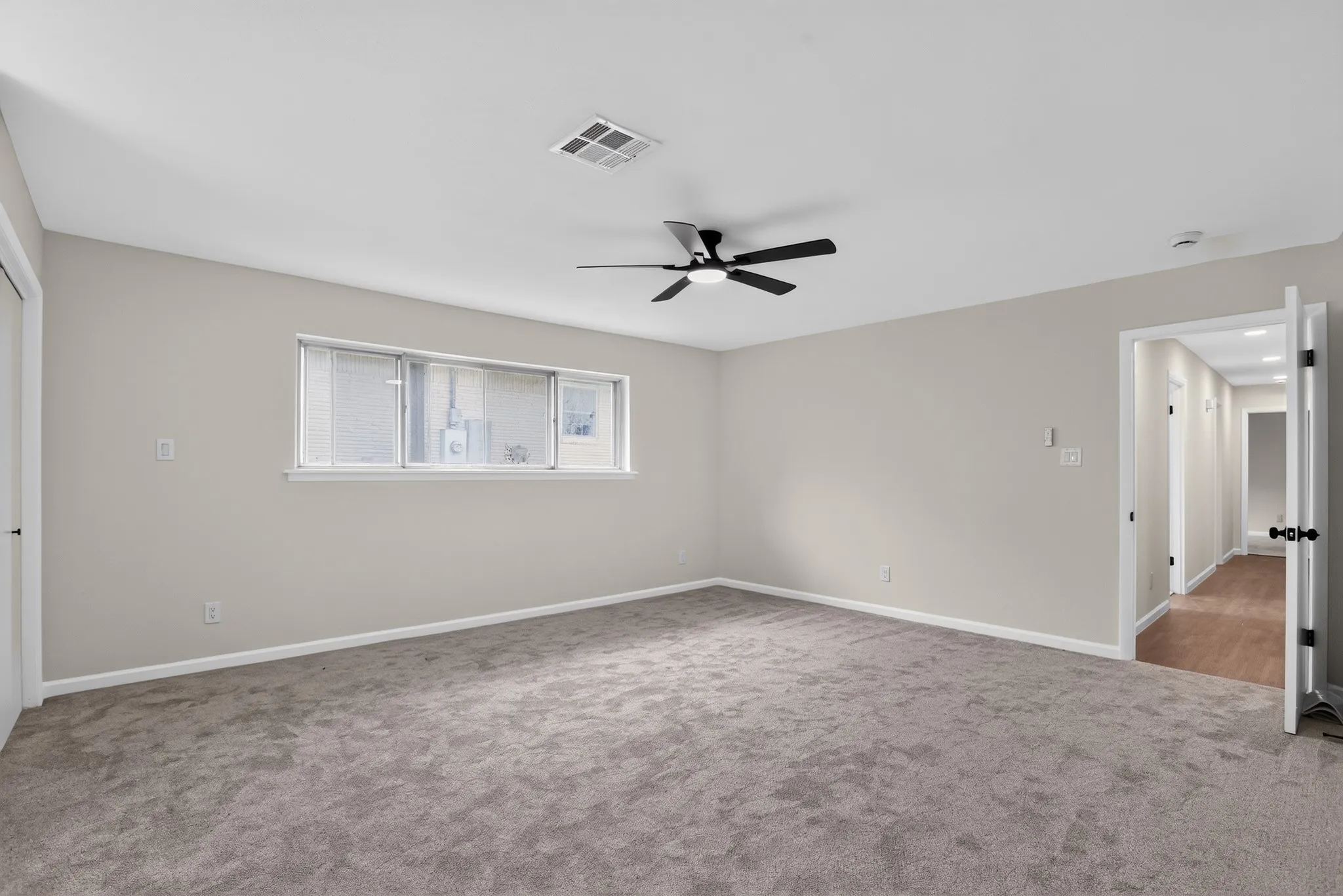 Spacious bedroom featuring neutral wall tones, large window with blinds, ceiling fan, and carpeted flooring