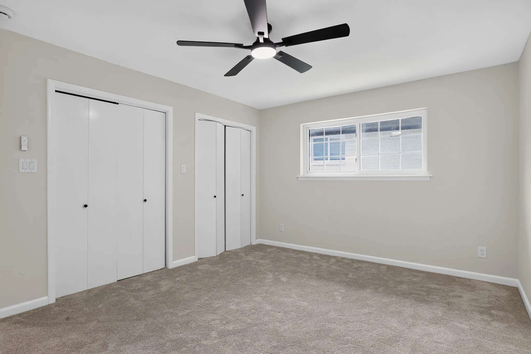 Neutral-toned walls and plush carpeting provide a versatile foundation for this space, complemented by a contemporary matte black ceiling fan with integrated lighting