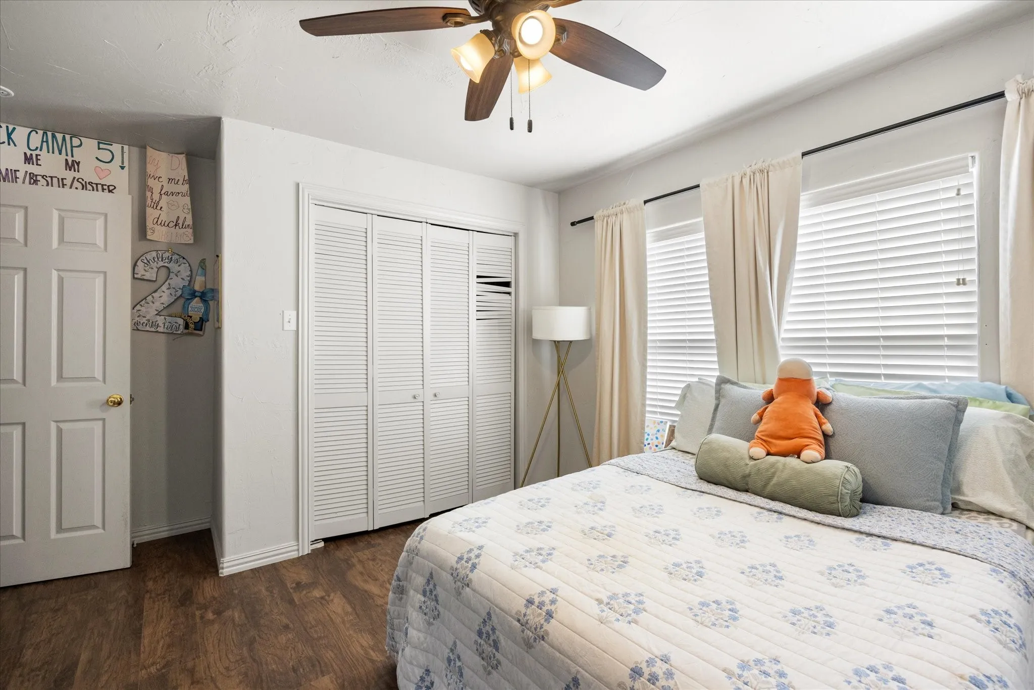 Bedroom featuring wood-finish flooring, a ceiling fan with integrated lighting, and multiple windows with blinds and curtain rods