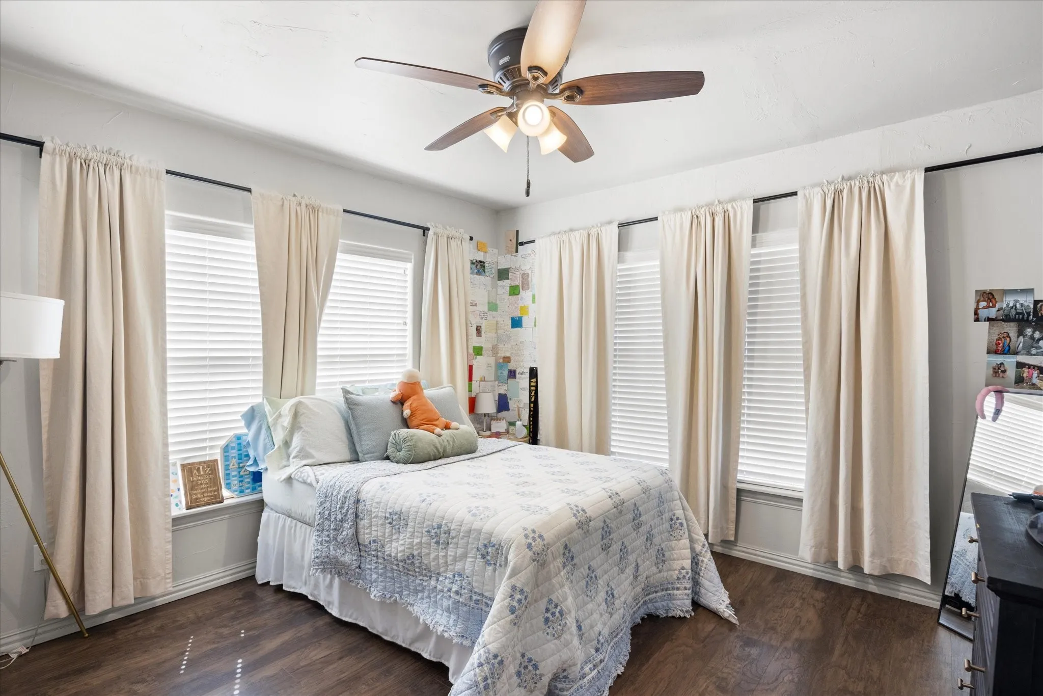 Room featuring wood-finish flooring, a ceiling fan with integrated lighting, and multiple windows with blinds and curtain rods