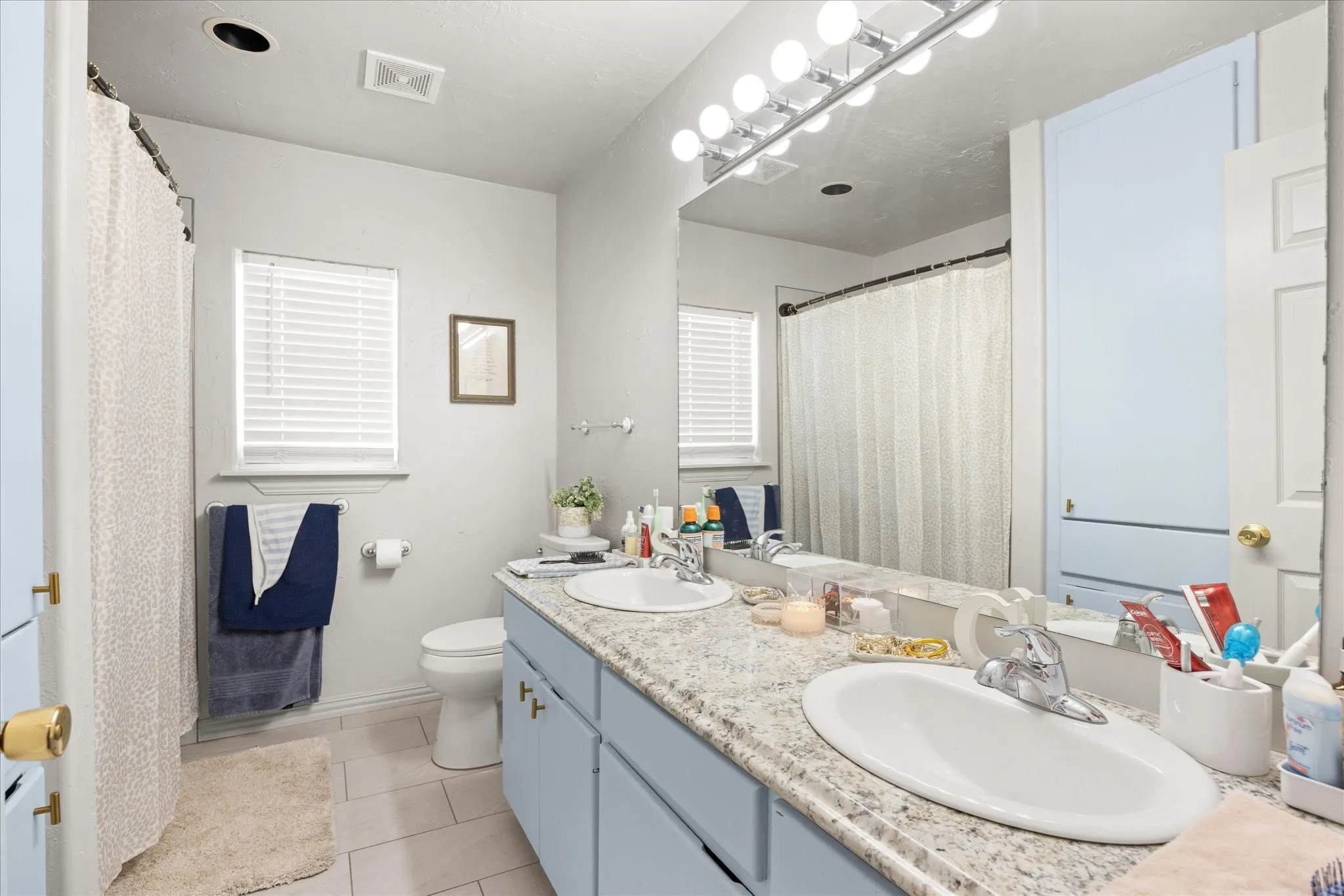 Bathroom featuring a double vanity with light blue cabinetry, dual undermount sinks, and a speckled countertop