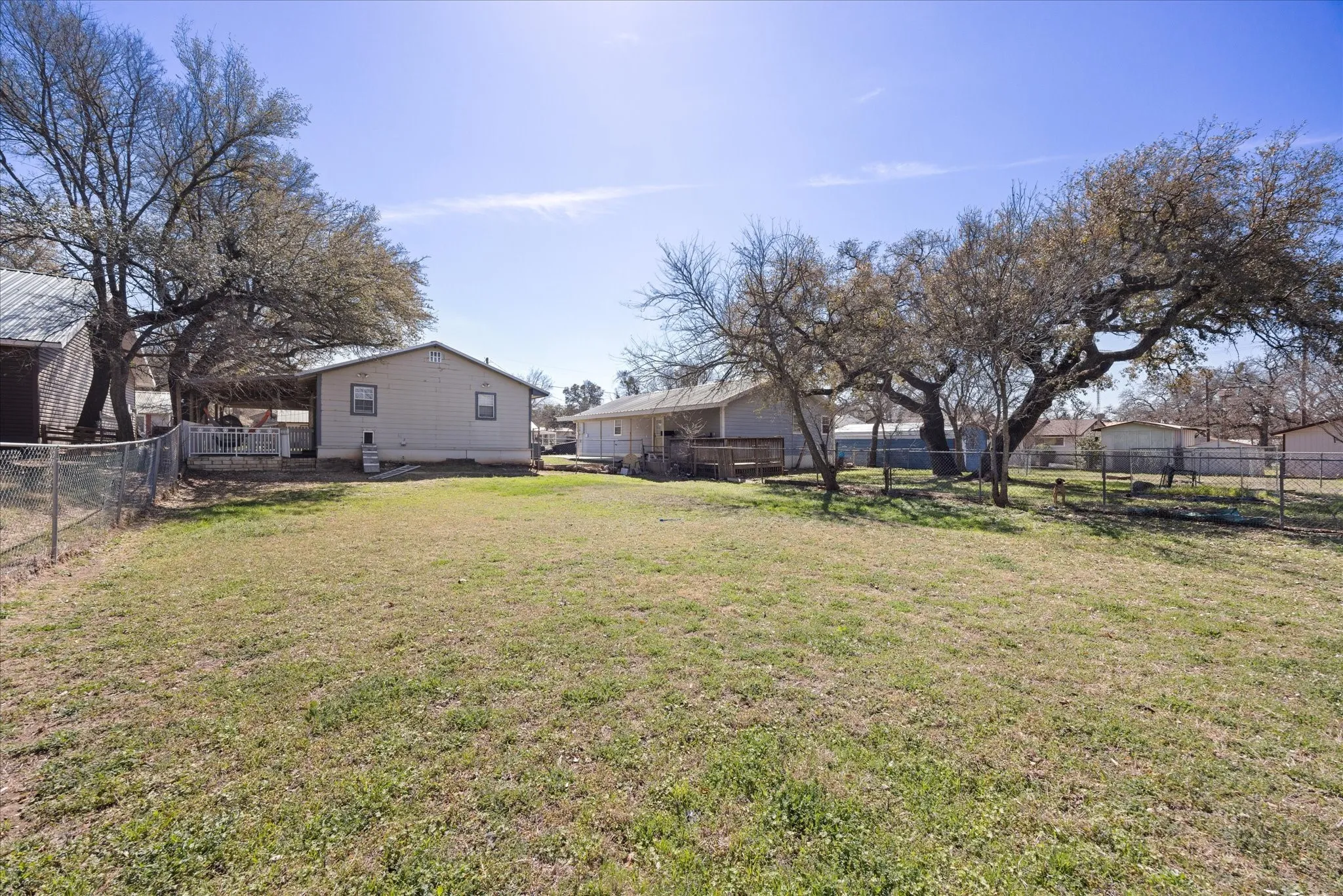 Expansive rear yard featuring mature trees and a chain-link fence